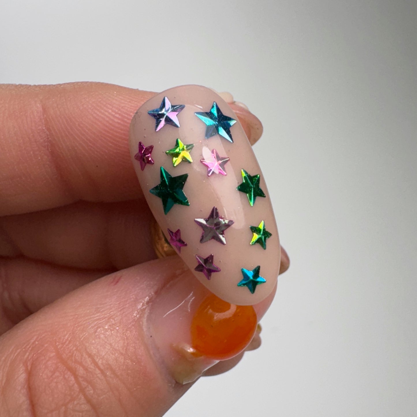 Hand holding decorated nail tip on light background.