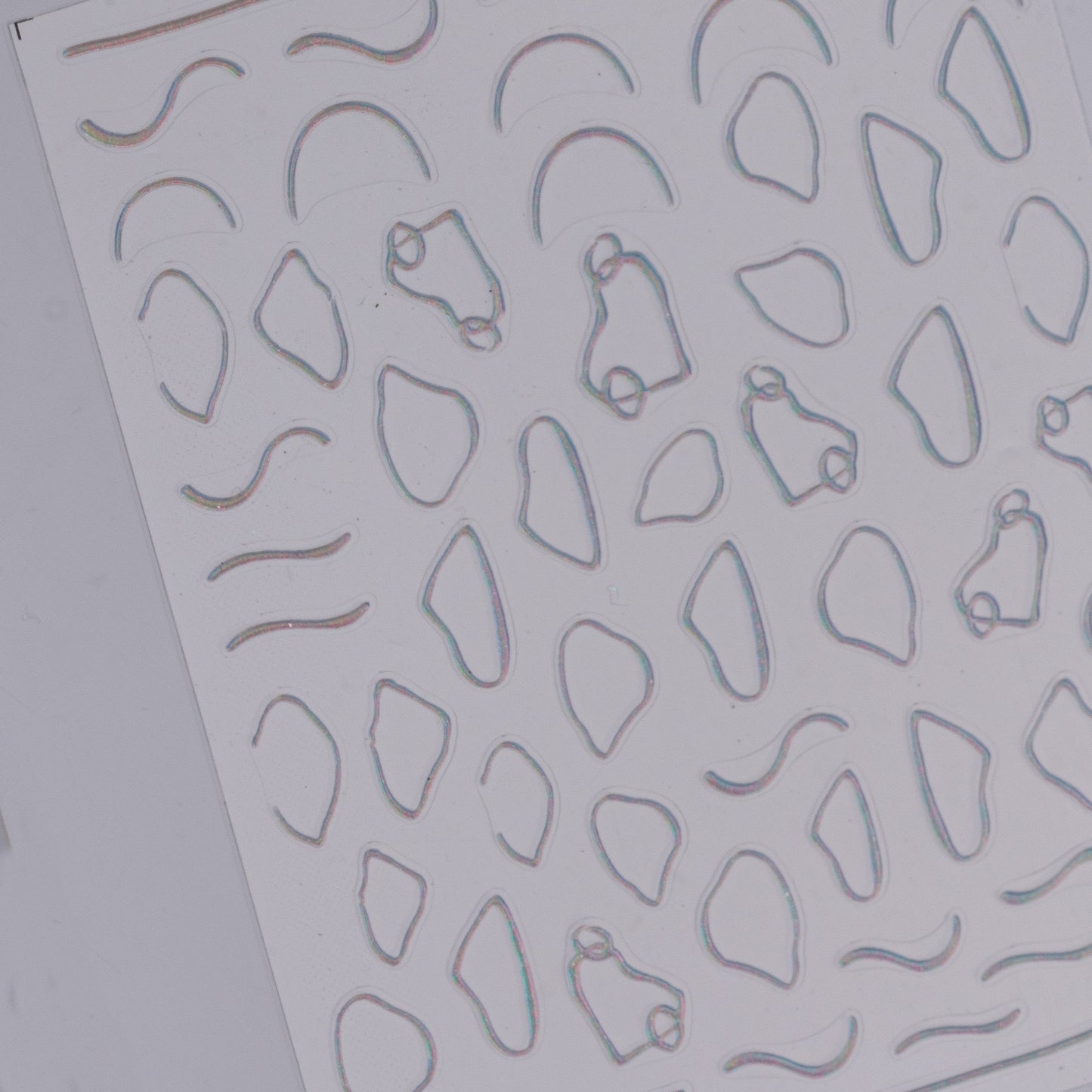 Sheet of embossed metal nail art stickerswith various geometric cutouts on a gray background