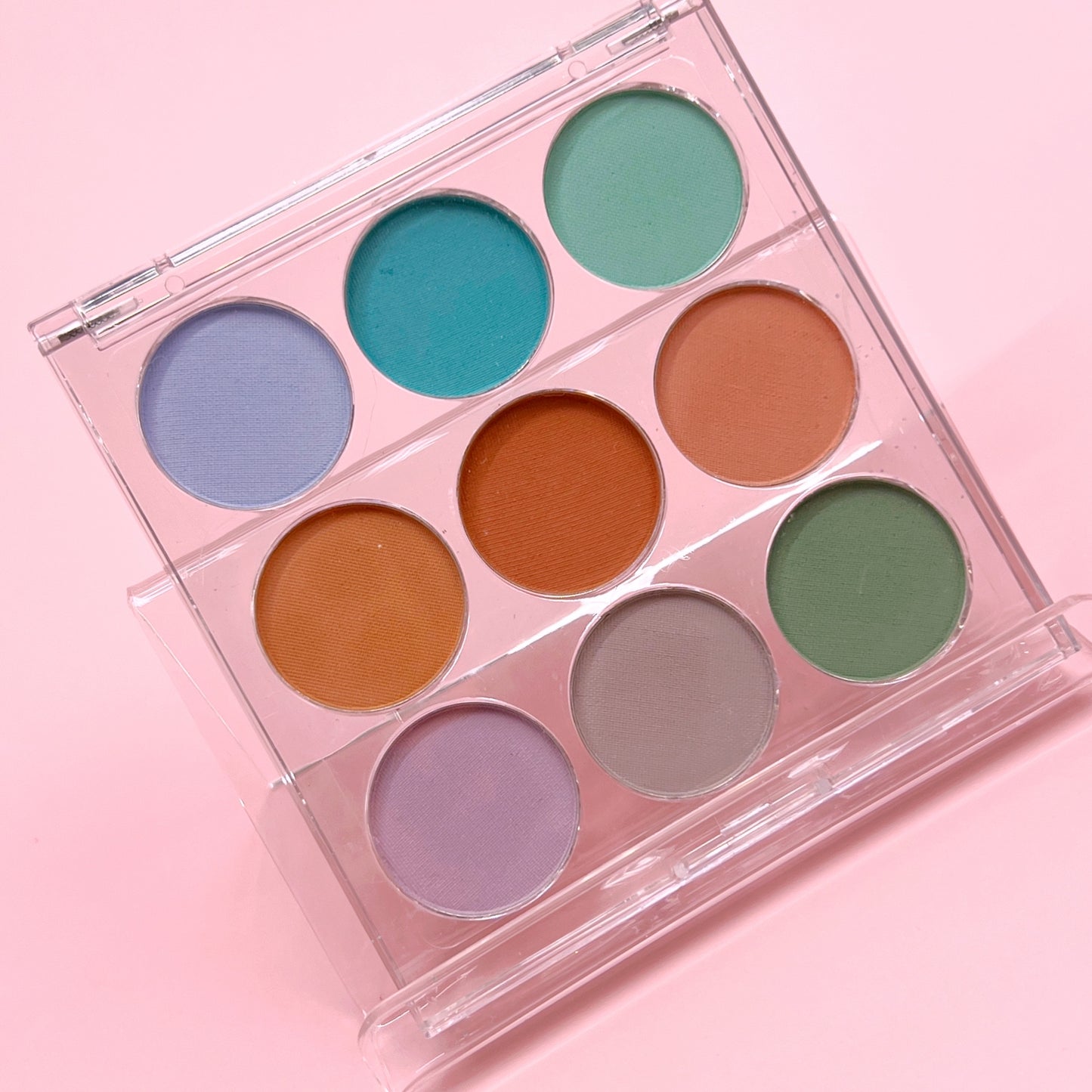 Multicolor pigment palette in clear case on pink background.