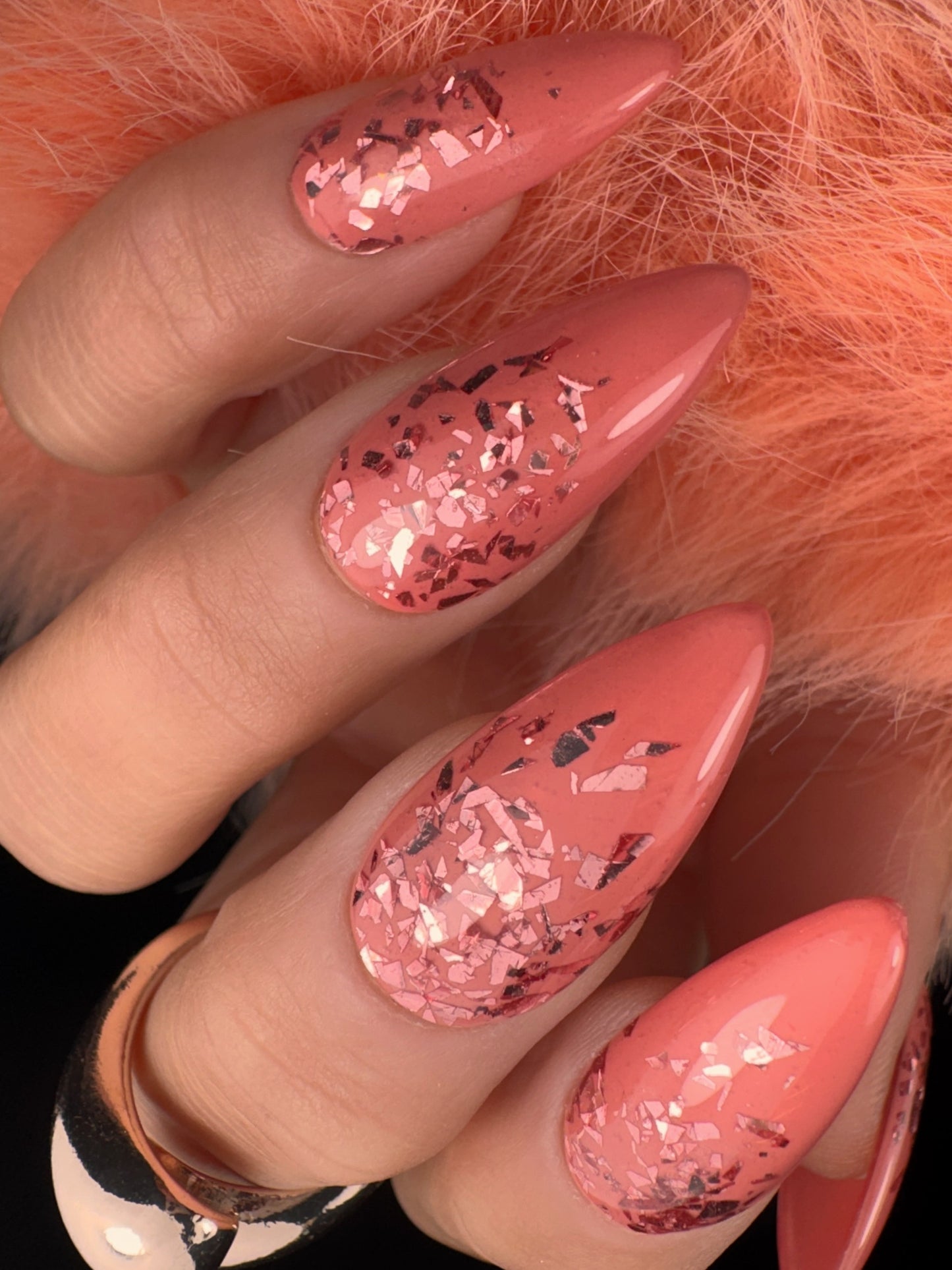 Close-up of a hand with pink glittery nails against a fluffy orange background