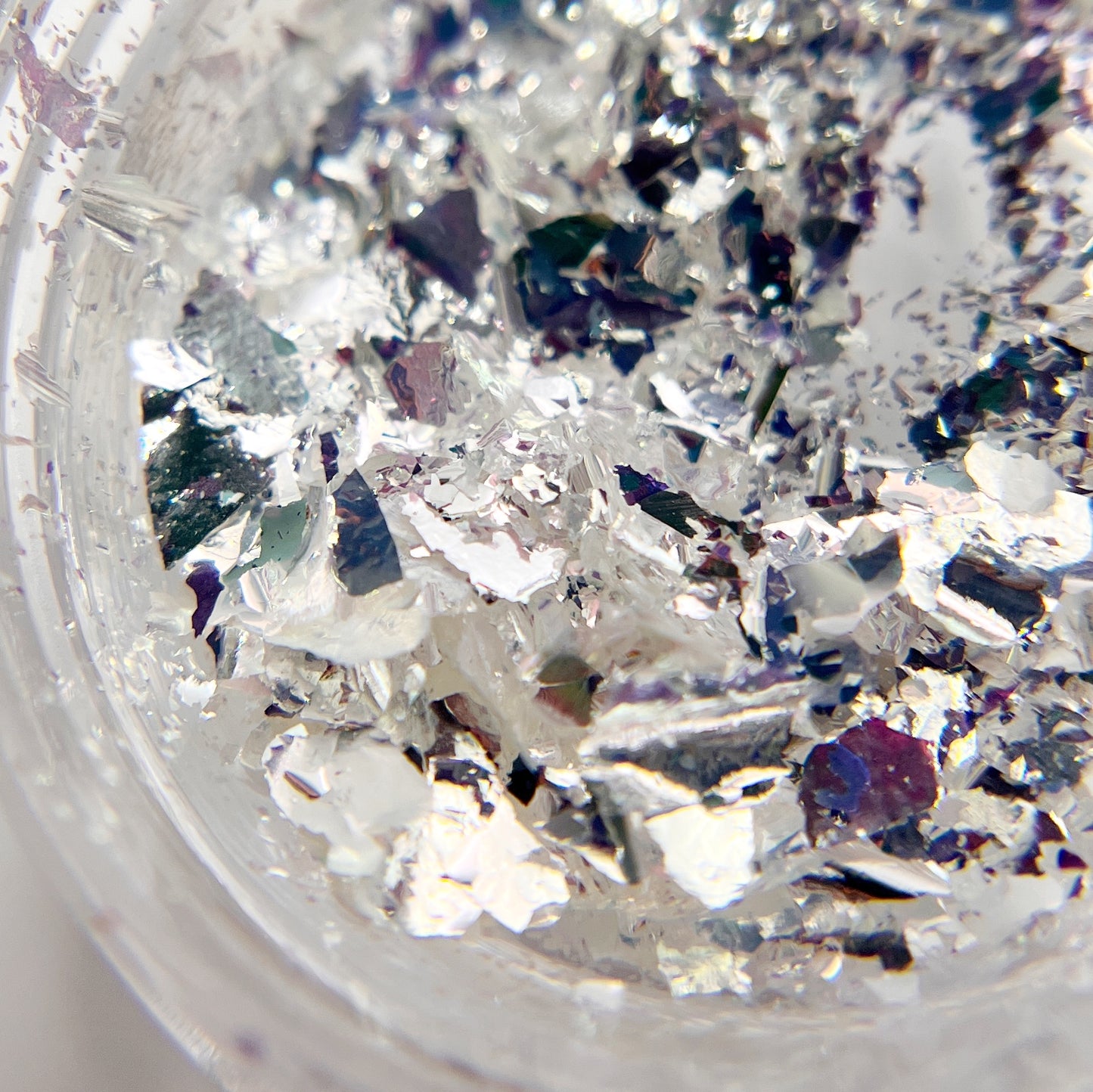 Detailed view of silver flakes in clear jar on white backgroud.