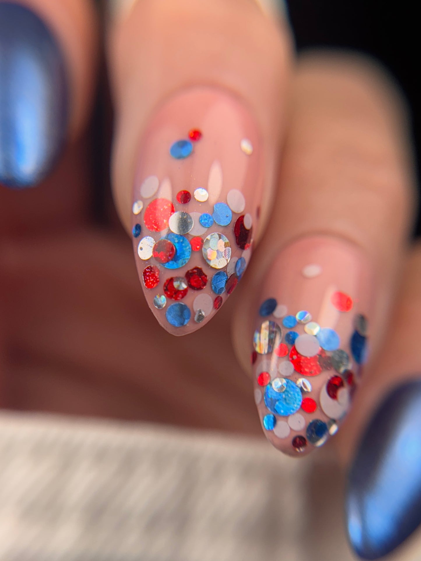 Nail art with colorful confetti glitter in red, silver and blue on a blurred background
