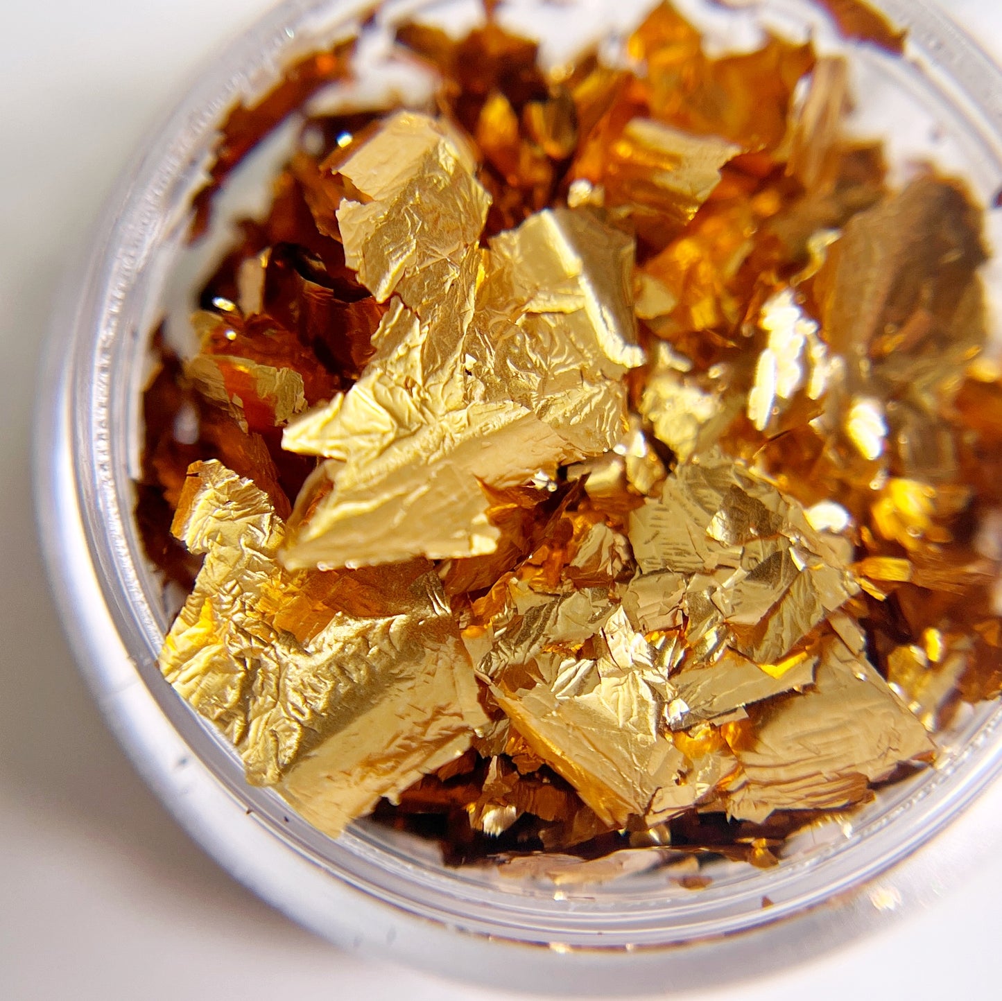 Detailed view: bronze foil flakes in clear jar on white background.