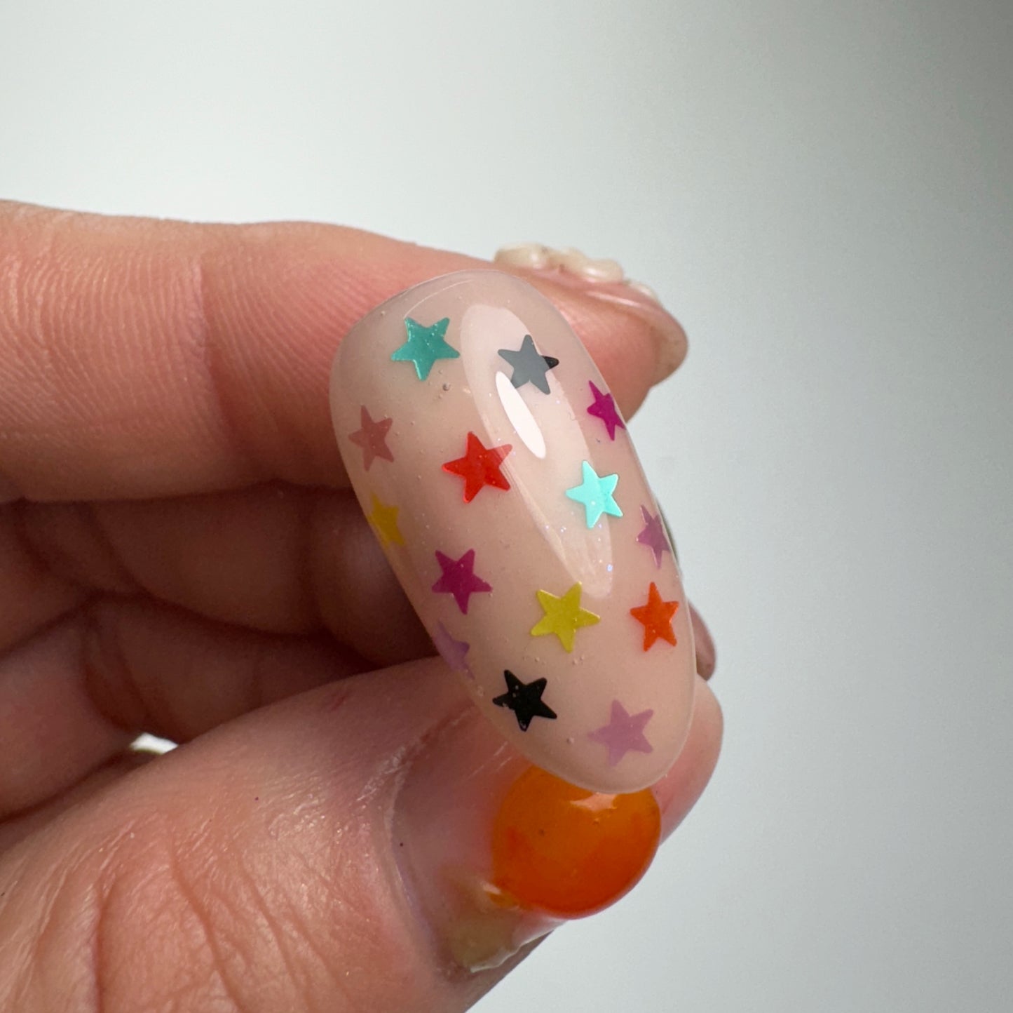 Hand holding decorated nail tip on light background.