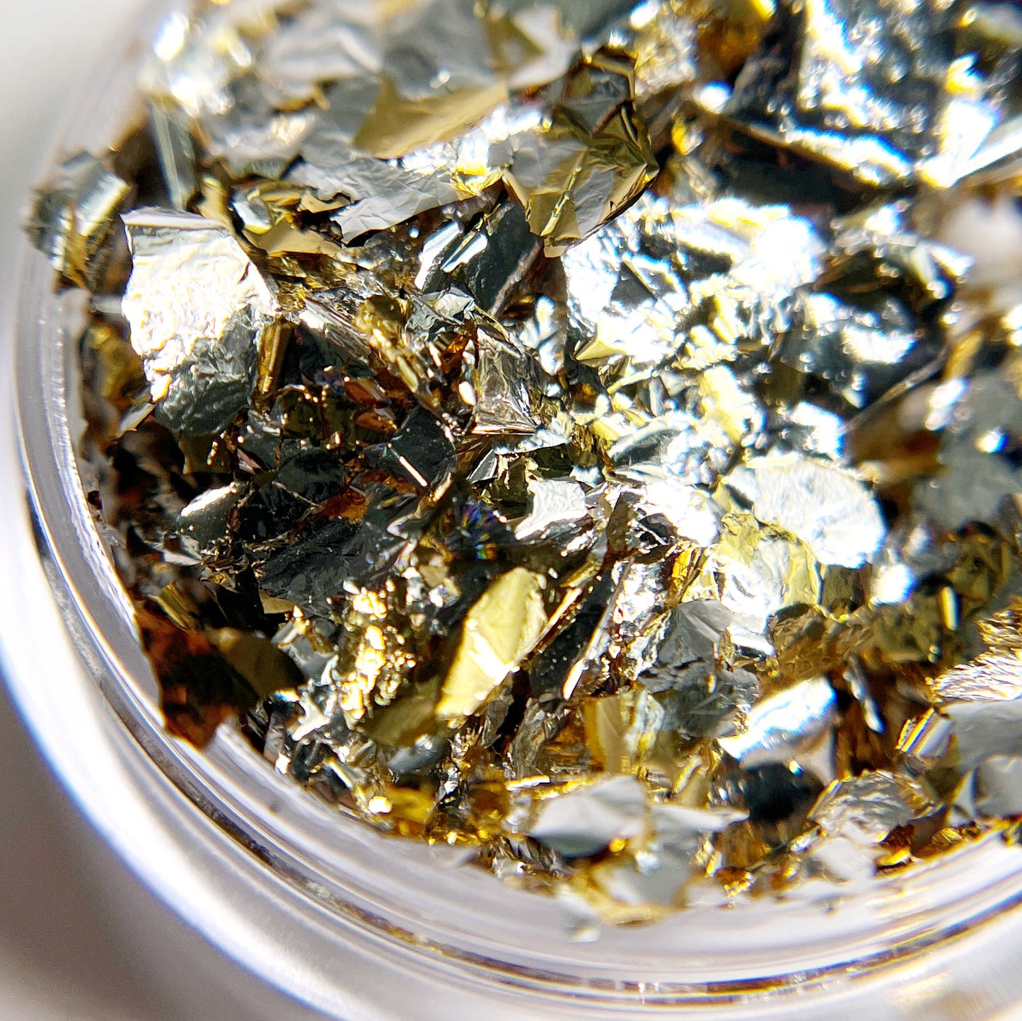 Detailed view of metallic flake in clear jar on white bakground.