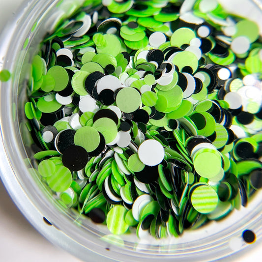 Multi-size green, black and white spots in clear jar on white background.