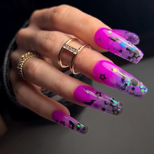 Hand with gold rings and long purple nails on a black background.