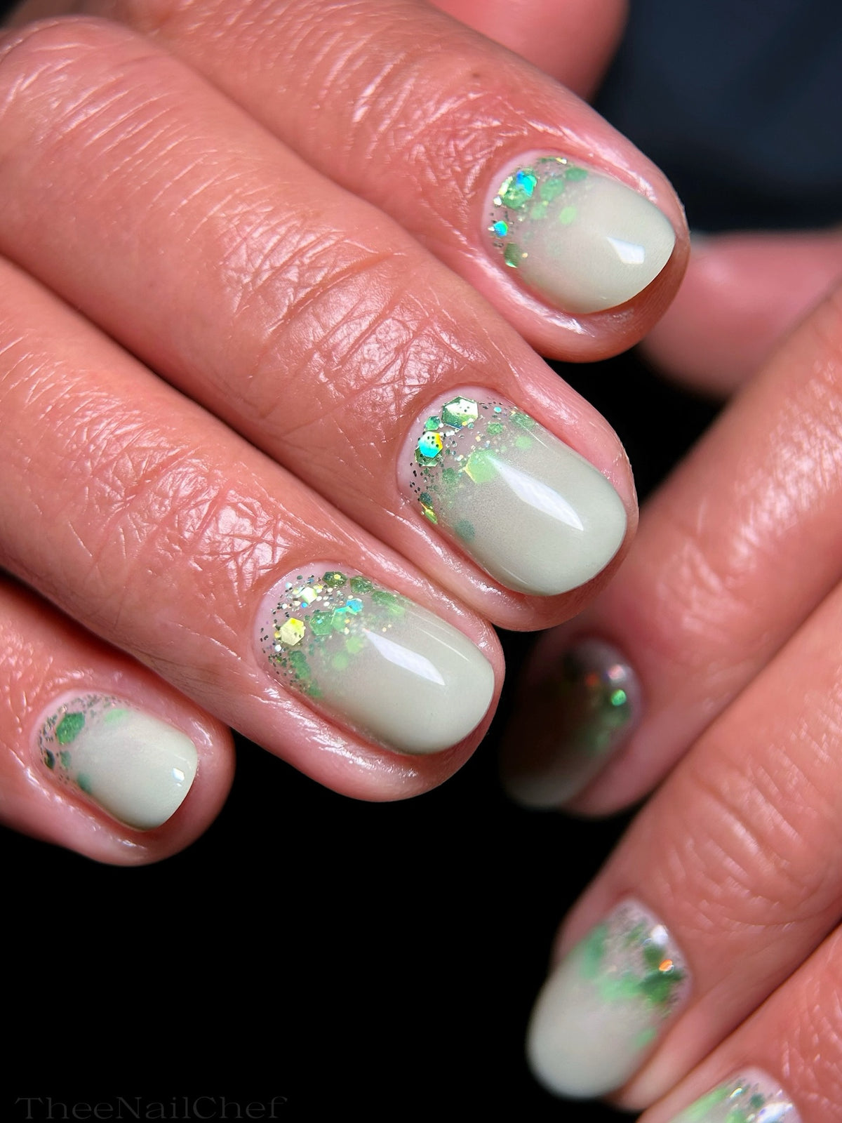 Pale sage green sparkly manicure by Jennie Guthrie featuring Vacation Nail Shop Green Party Glitter scattered along the cuticles, with iridescent green hex glitter.