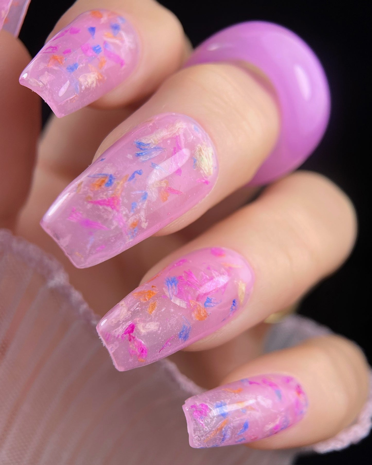 Close-up of a hand with pink gel nails featuring colorful flowers on a dark background