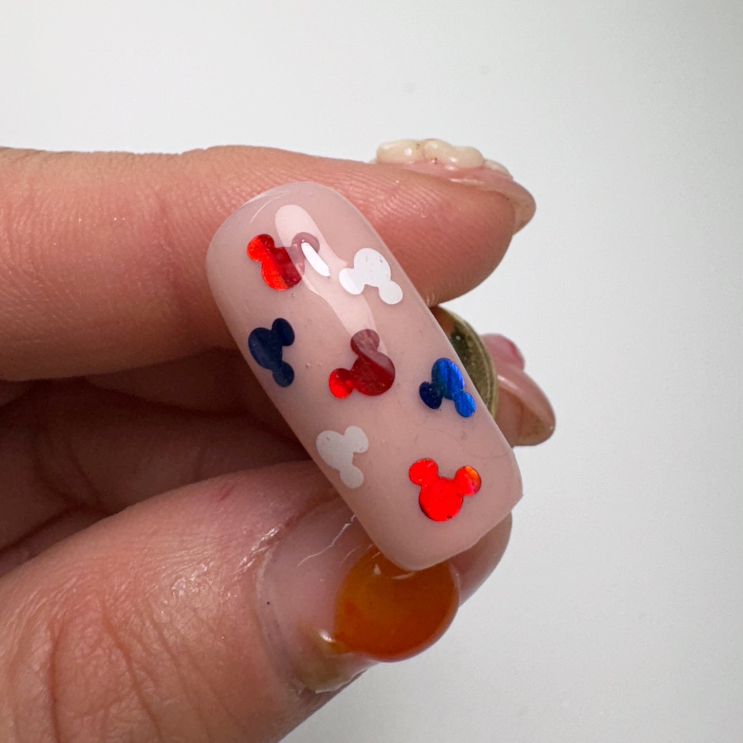 Hand holding decorated nail tip against light background.