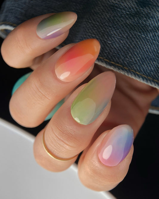Nails with gradient colors on manicured hand wearing a gold ring.