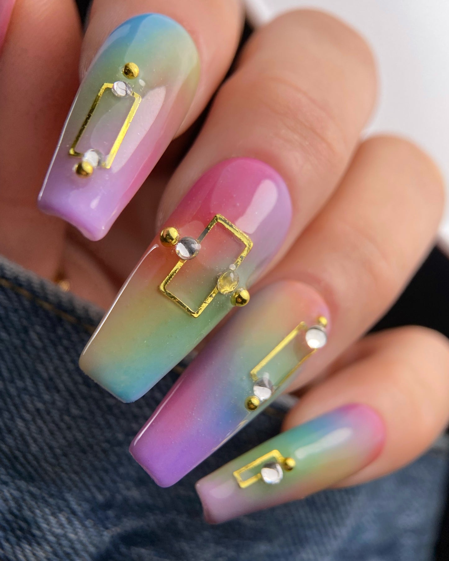 Multicolored nail art with gold and silver decorations on a denim background