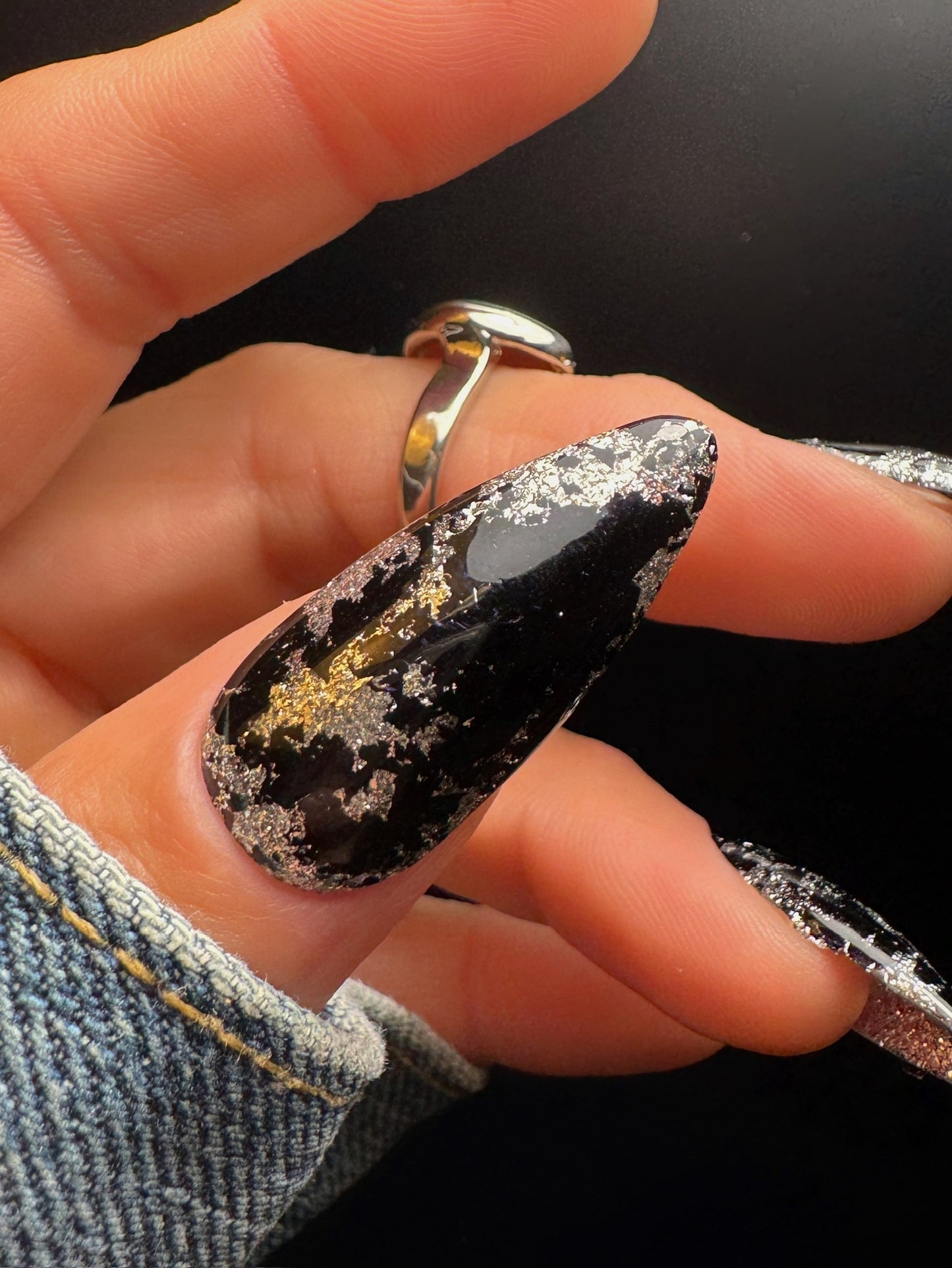 Close-up of a hand with black and silver nail design on a dark background