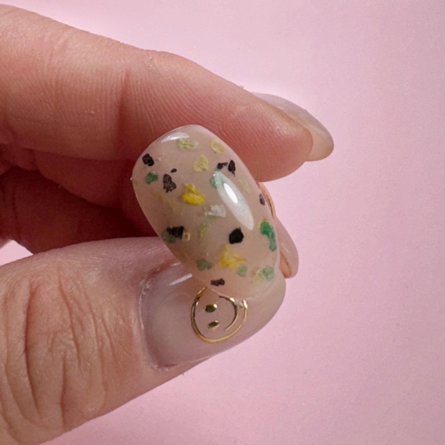 Close-up of a hand holding decorated nail tip on pink background