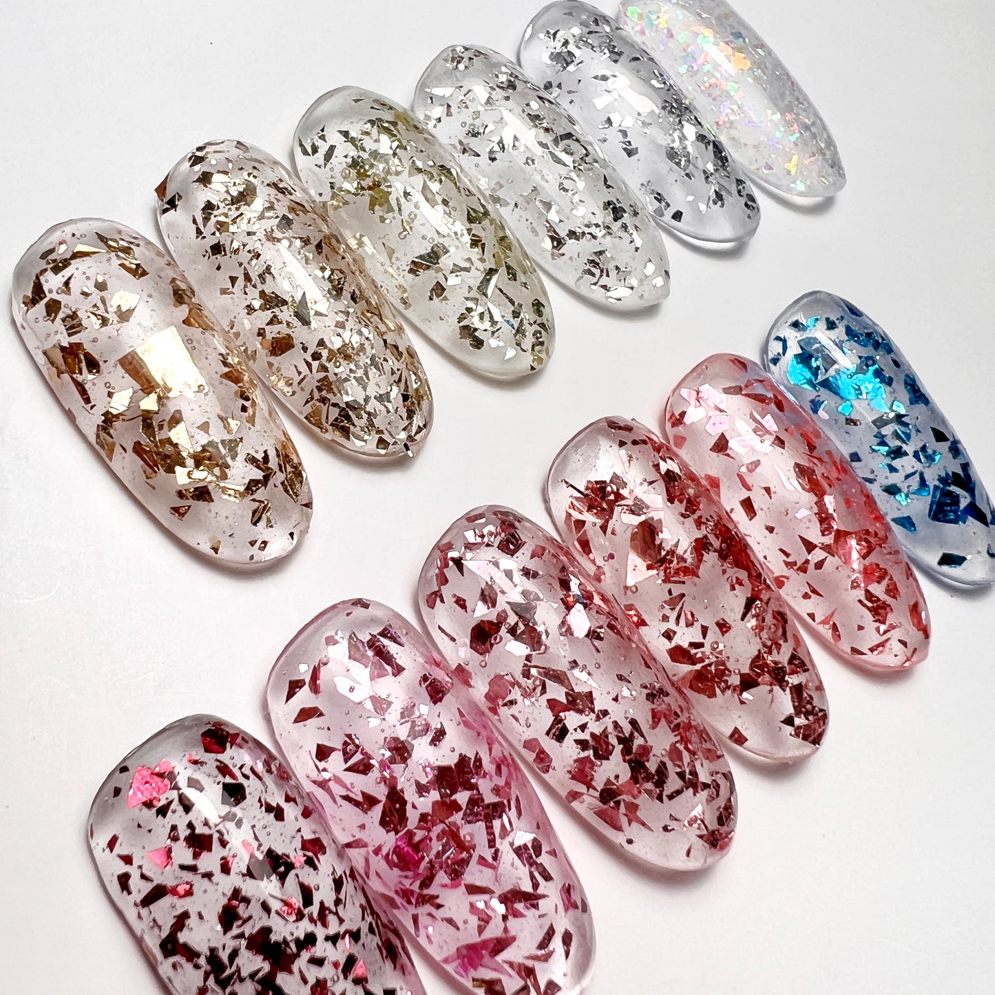 A collection of nail art images showing a variety of fleck glitter designs in different colors, including blue, pink, and silver on transparent nail tips on white background.