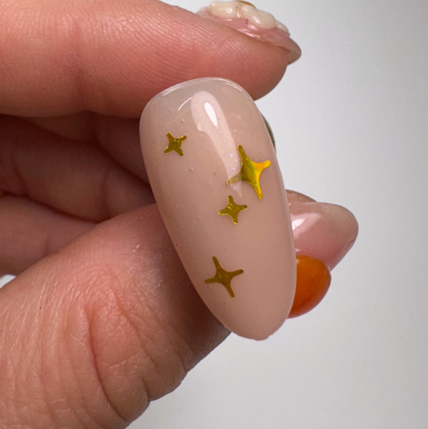 Hand holding decorated nail tip against light background.