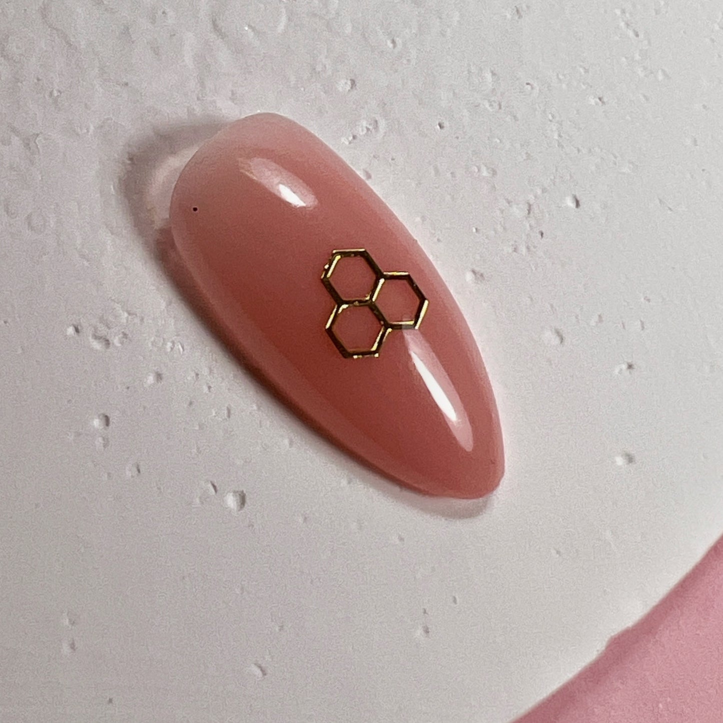 Pink nail with gold hexagonal design on a light gray background