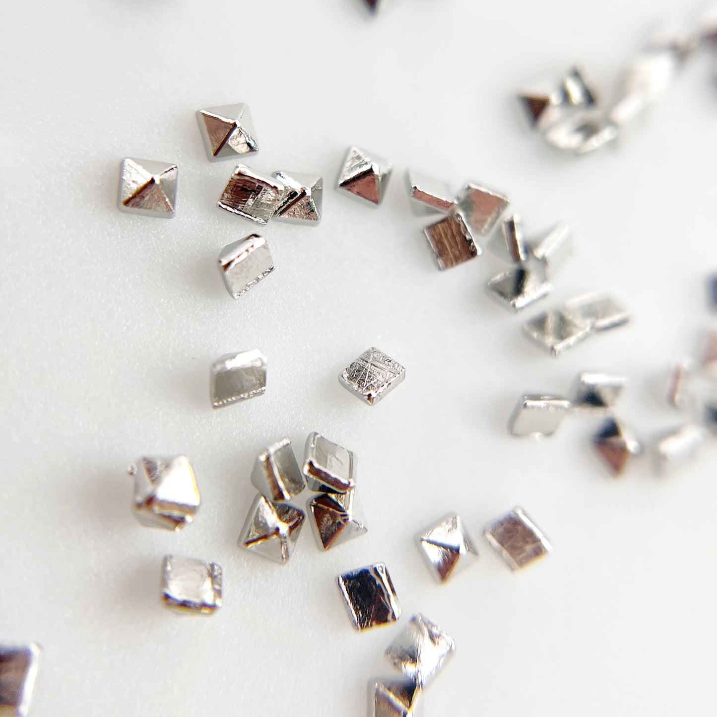 Silver pyramid studs scattered on white background.