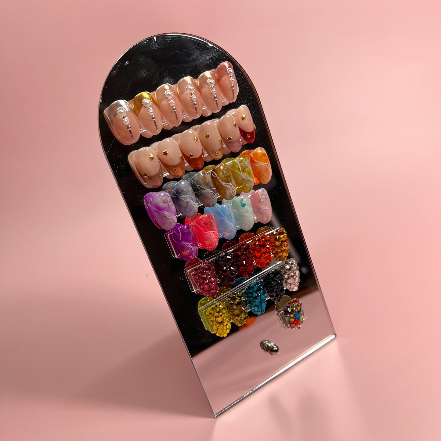 Photo of mirrored nail art display wth tips on pink backdrop.