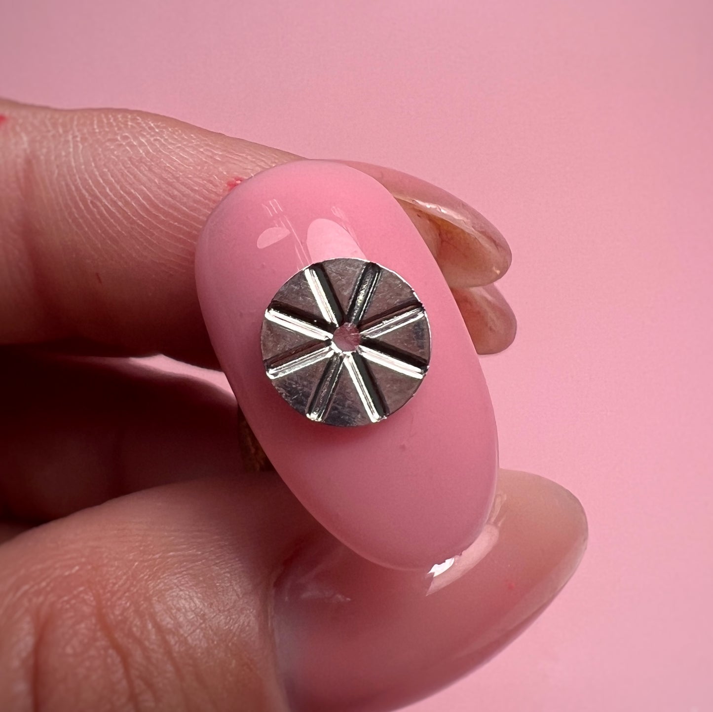 Pink nail with a silver decorative element held between fingers against a pink background