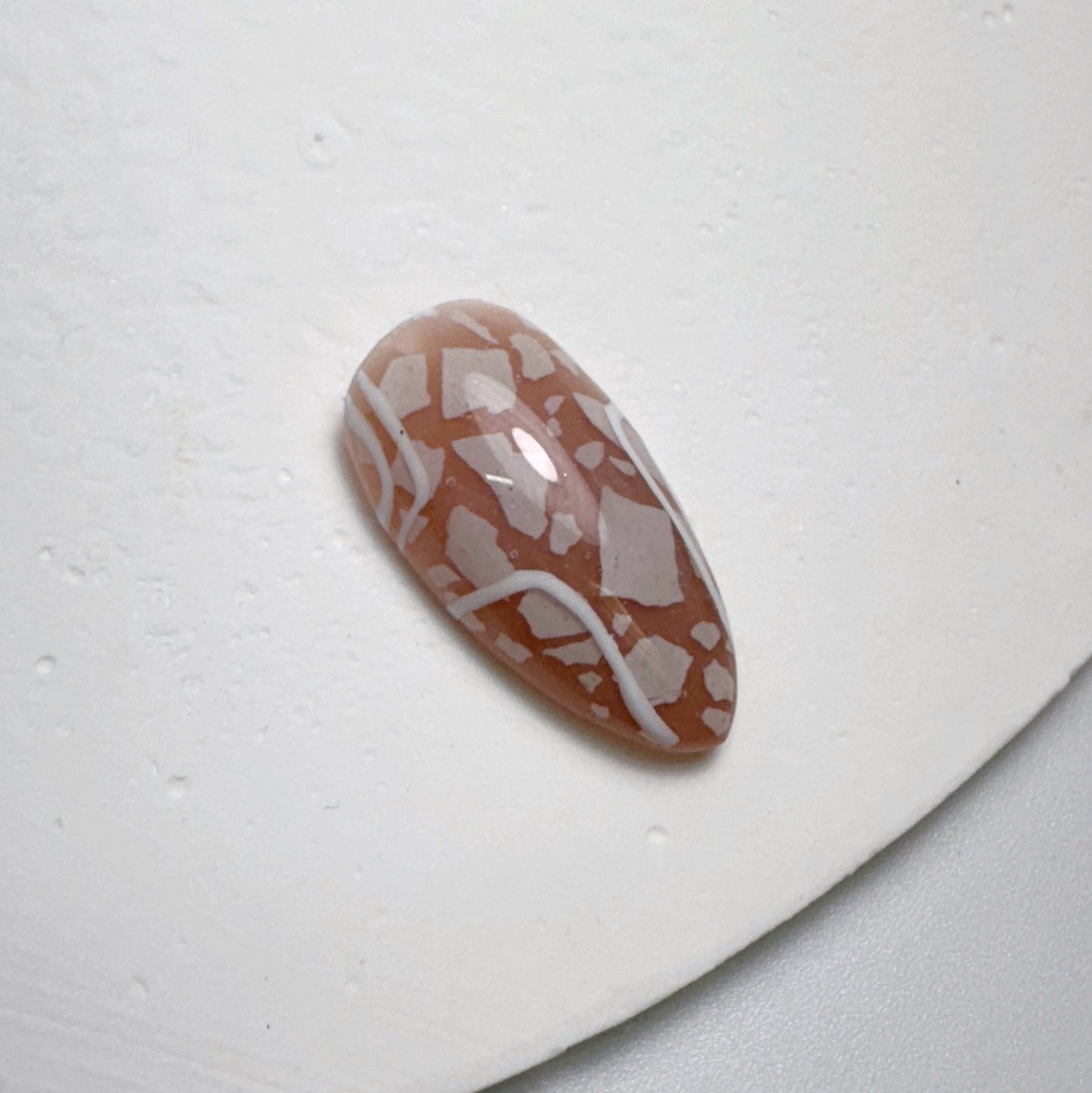 Decorated nail tip on white textured surface.