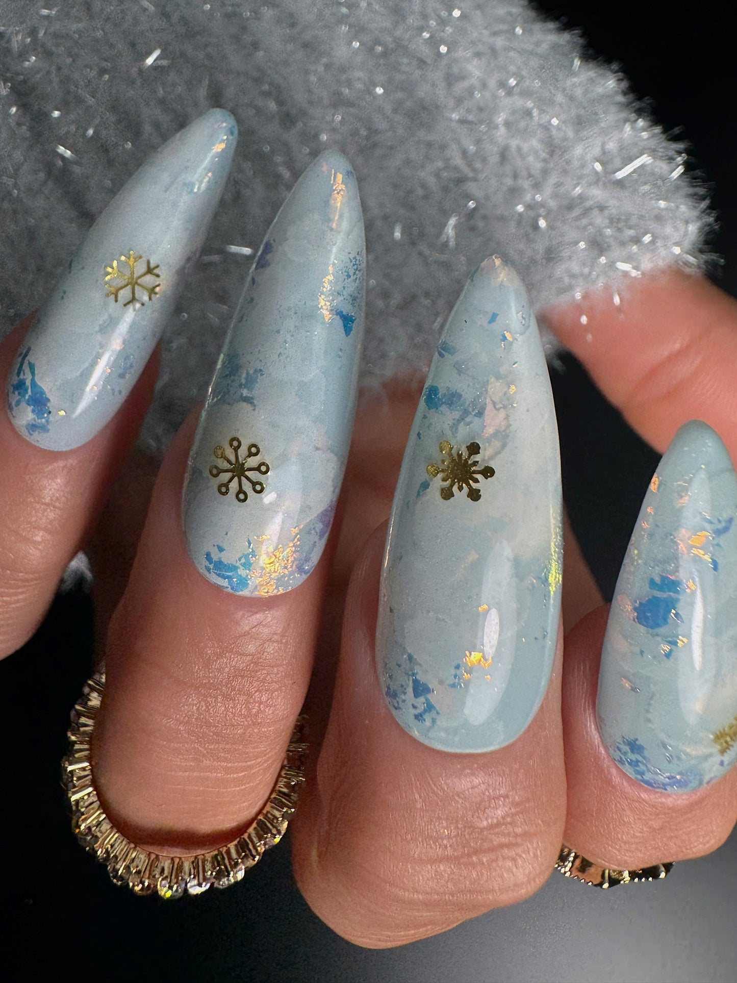 Nails with light blue and gold snowflake design on a textured black background