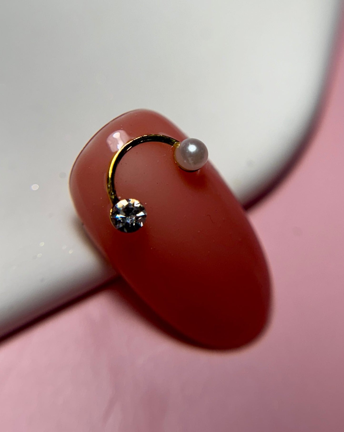 Close-up of nail tip with gold charm with a pearl on a white and pink surface