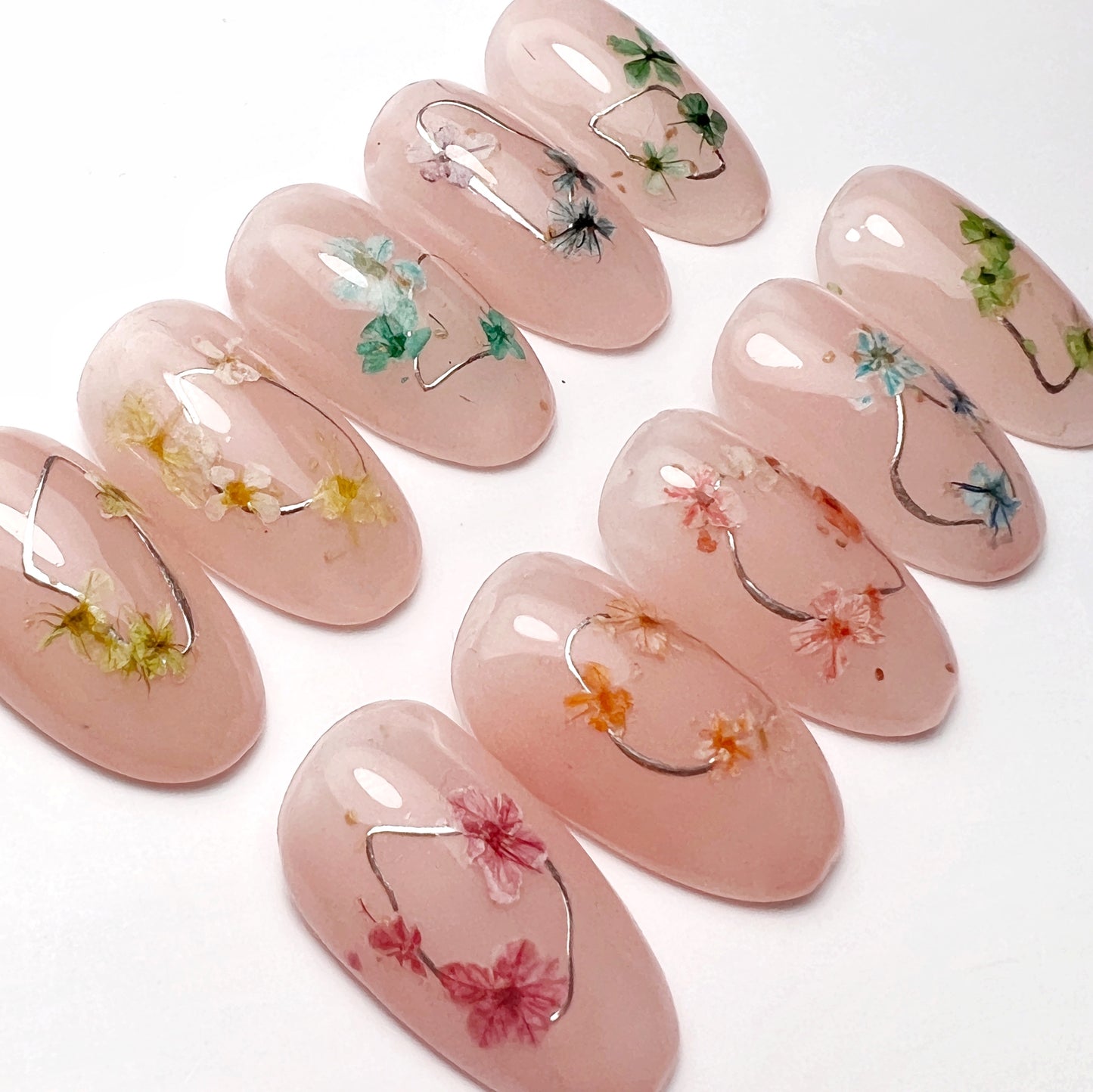 A collection of nail art tips with artificial flowers in various colors, arranged on a surface to demonstrate variety and color range.