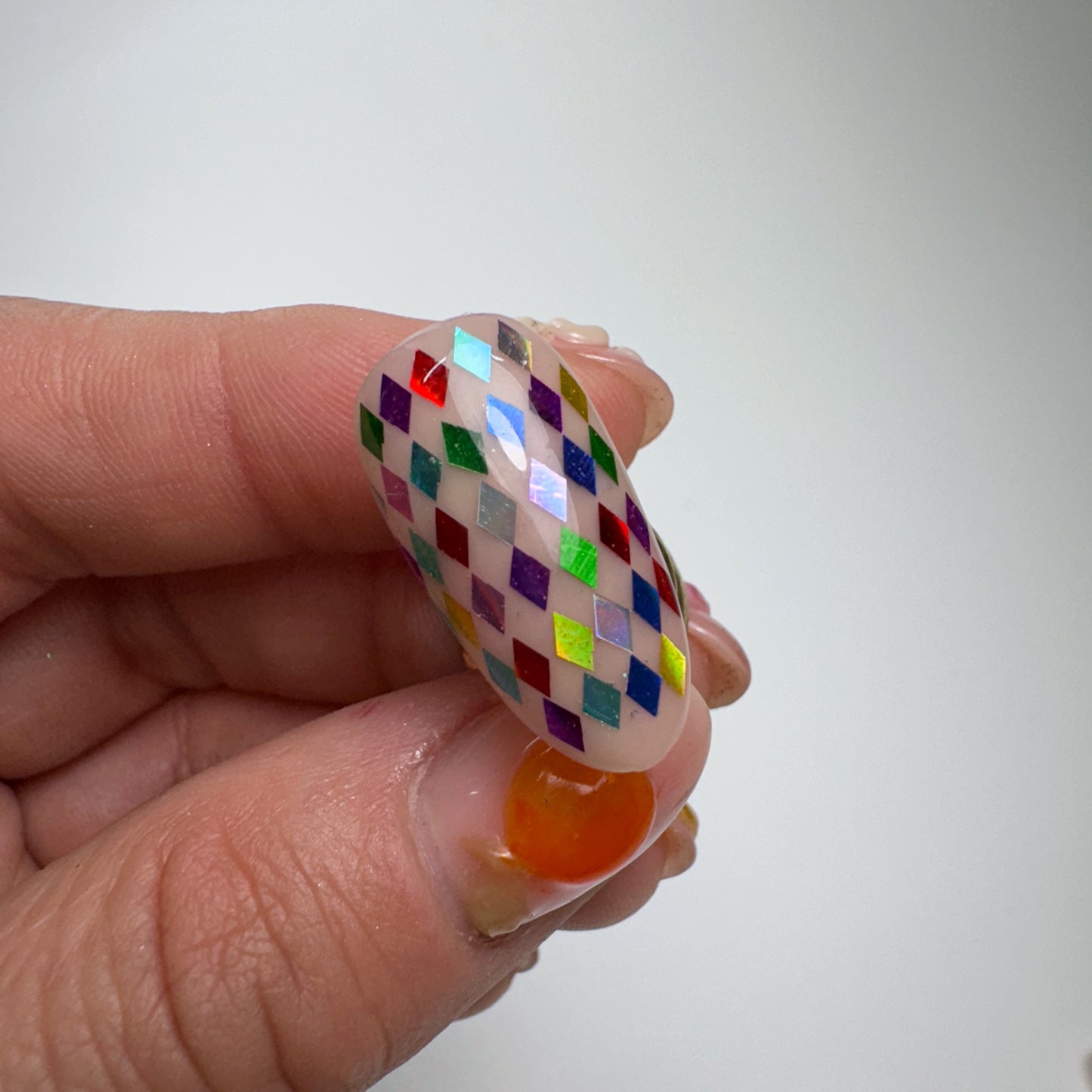 Hand holding decorated nail tip on light background.