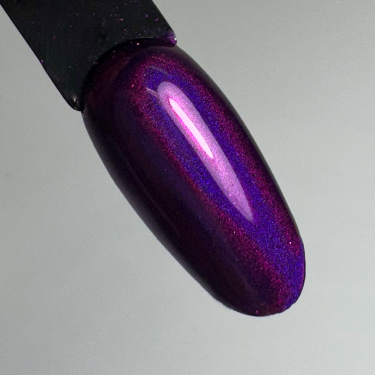 Black nail swatch stick with metallic purple finish held against light background.