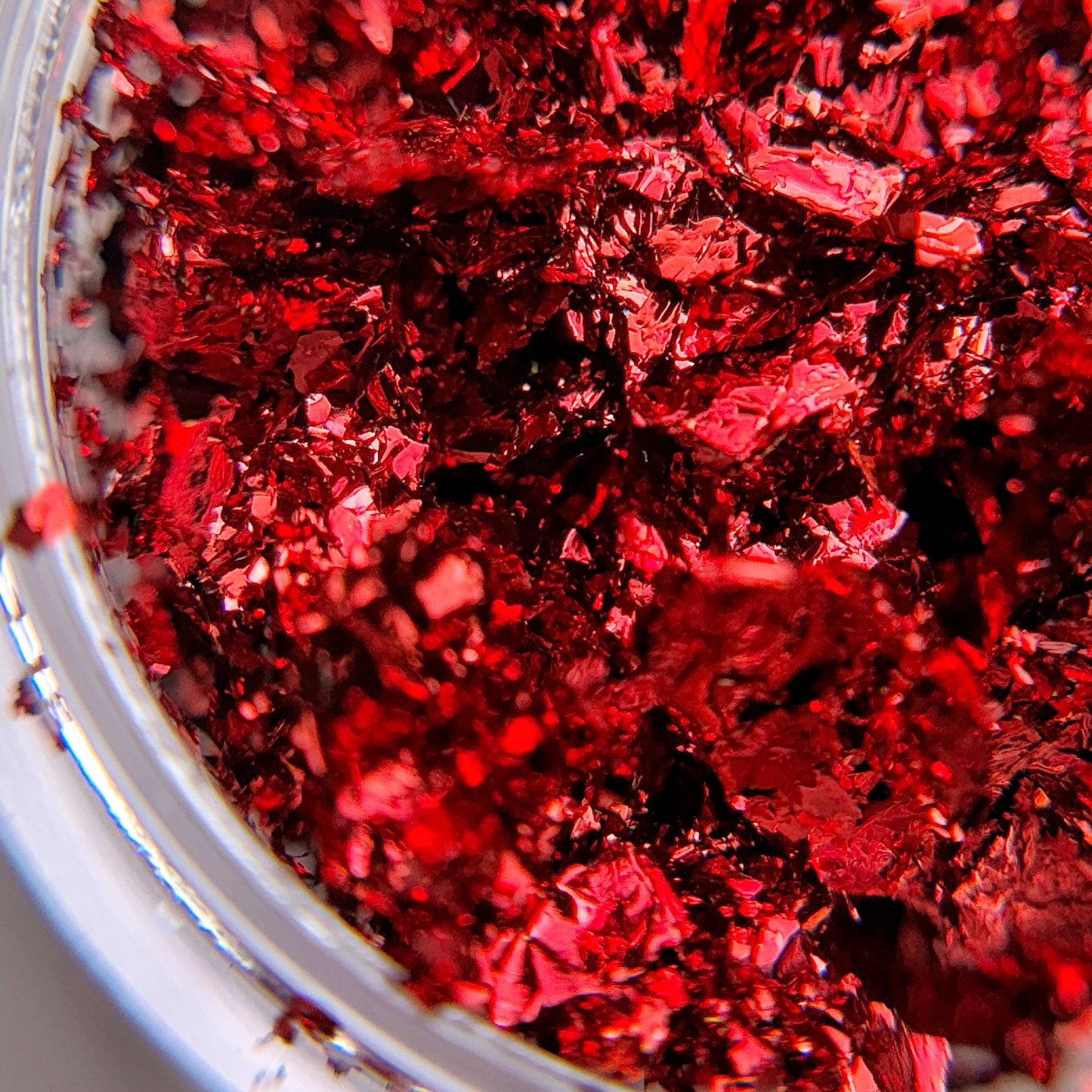 A close-up view of red metallic nail art flakes scattered around, likely used for creating glittery designs on nails.
