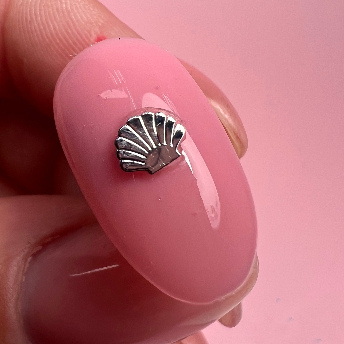 Silver shell charm on a pink nail with a pink background
