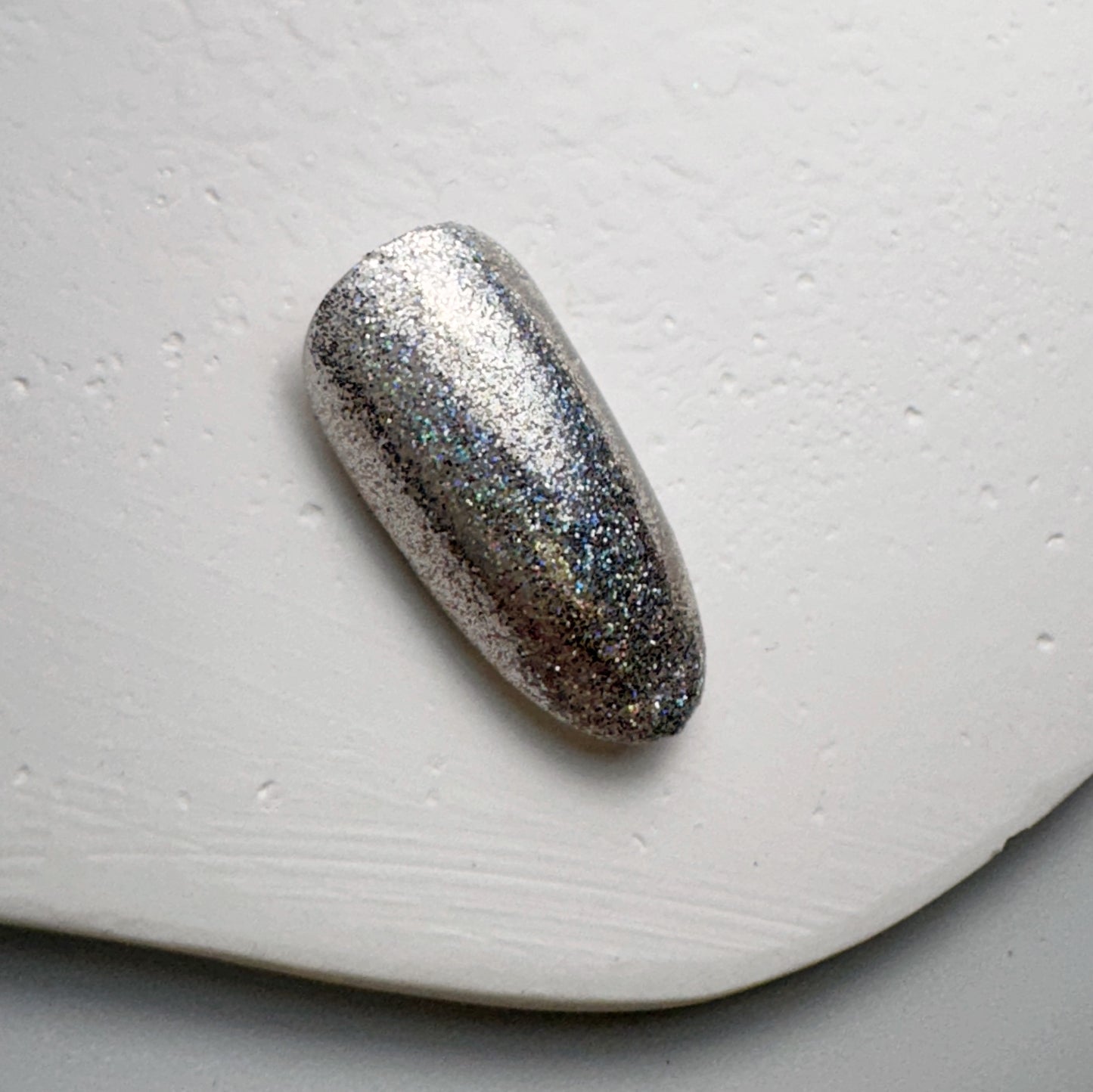 Glittery nail tip on white textured surface.