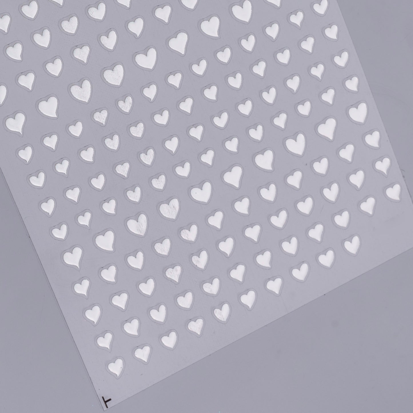 Sheet of silver heart-shaped stickers on a gray background
