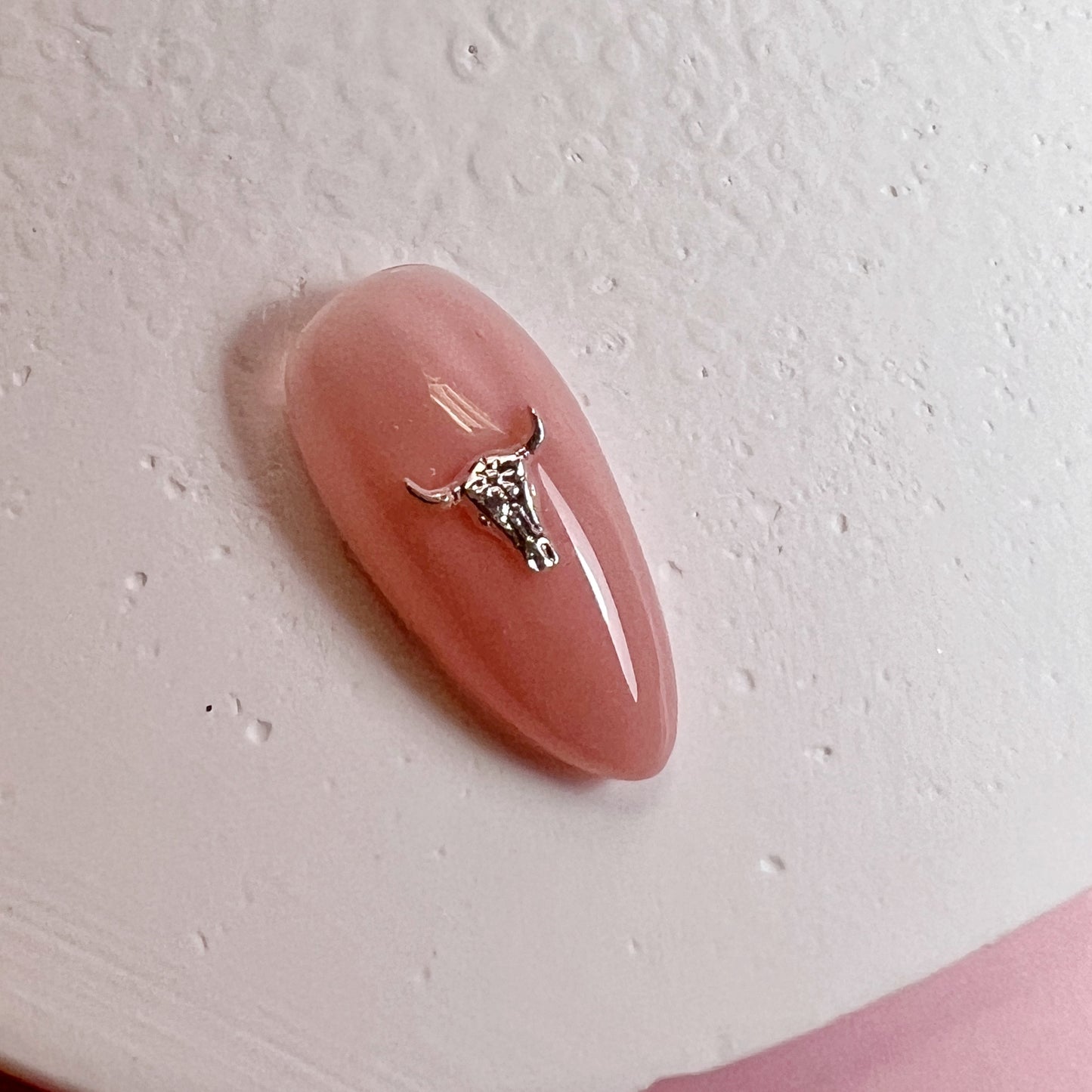Pink nail with a small metallic charm on a light pink background
