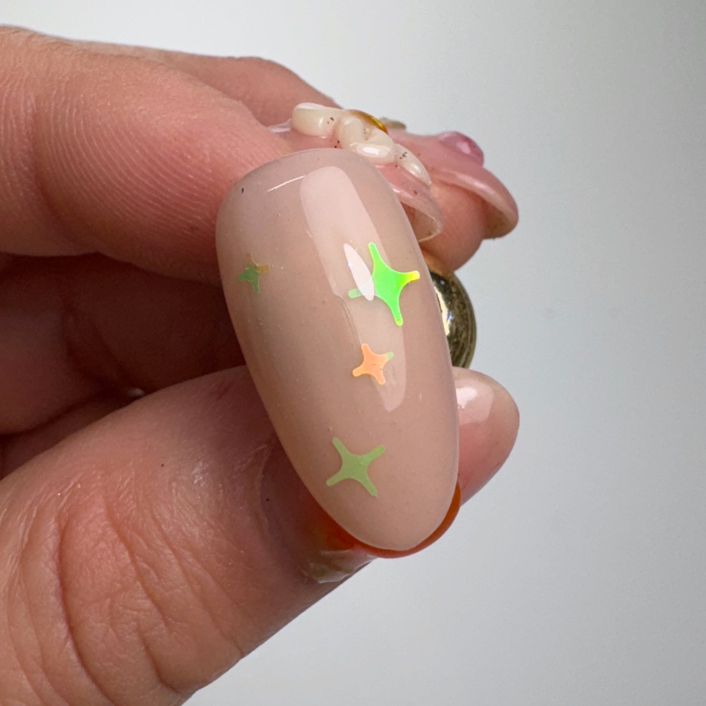Hand holding decorated nail tip against light background.