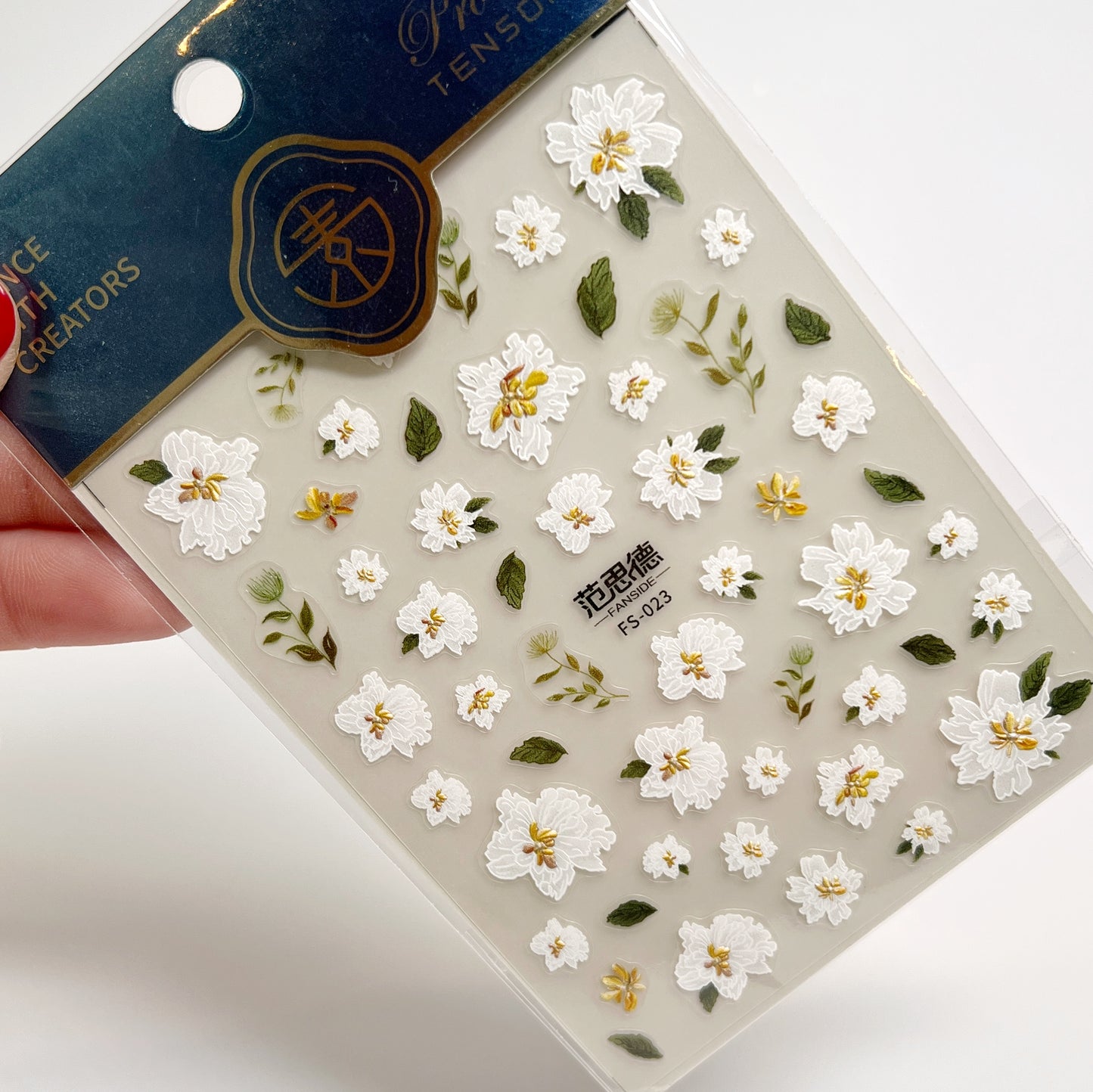 Floral nail sticker sheet held by a hand with a brand label in the background