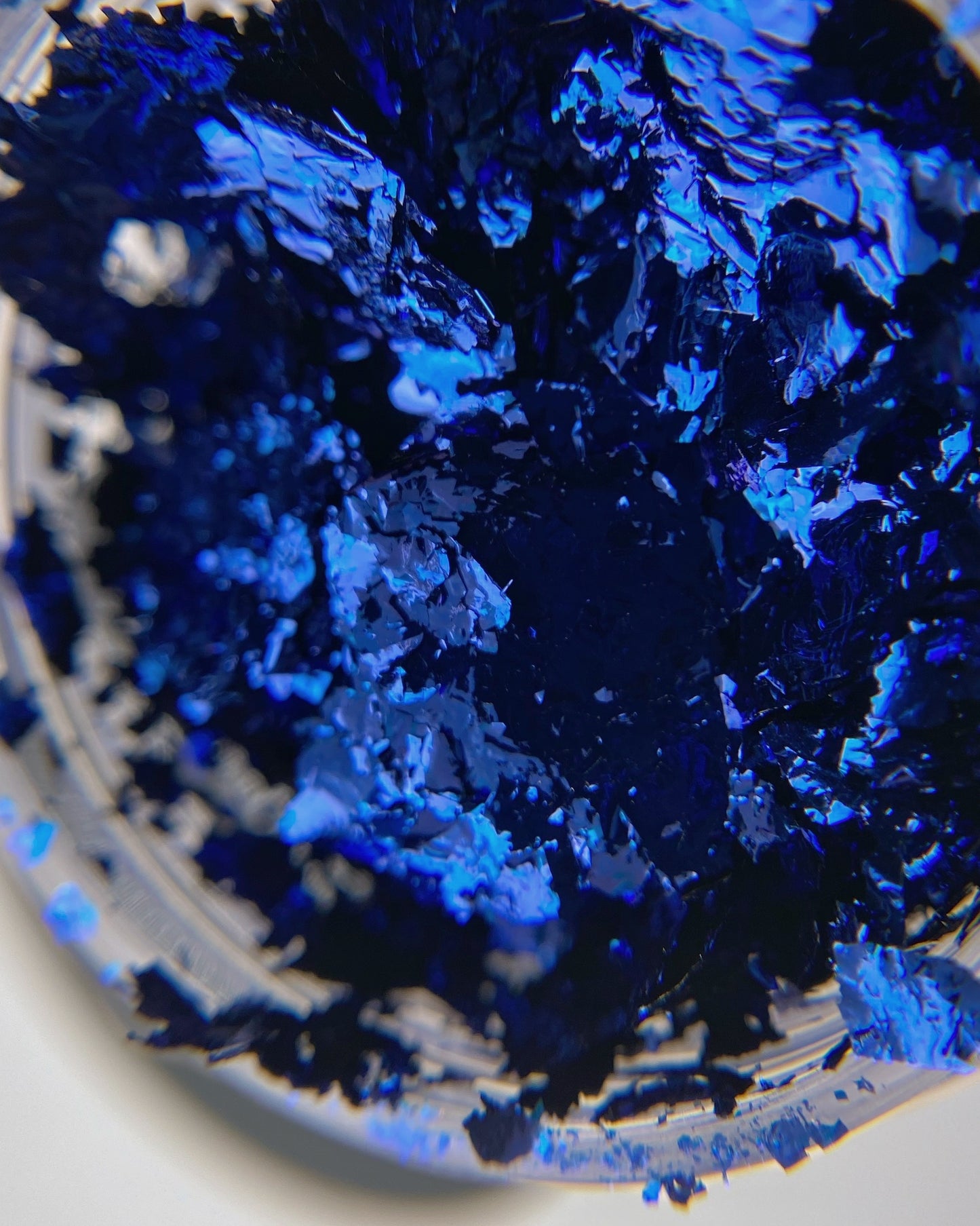 Macro close-up of Vacation Nail Shop Navy Foil Flakies, showing irregular metallic flakes with a deep navy base and vivid blue reflection.