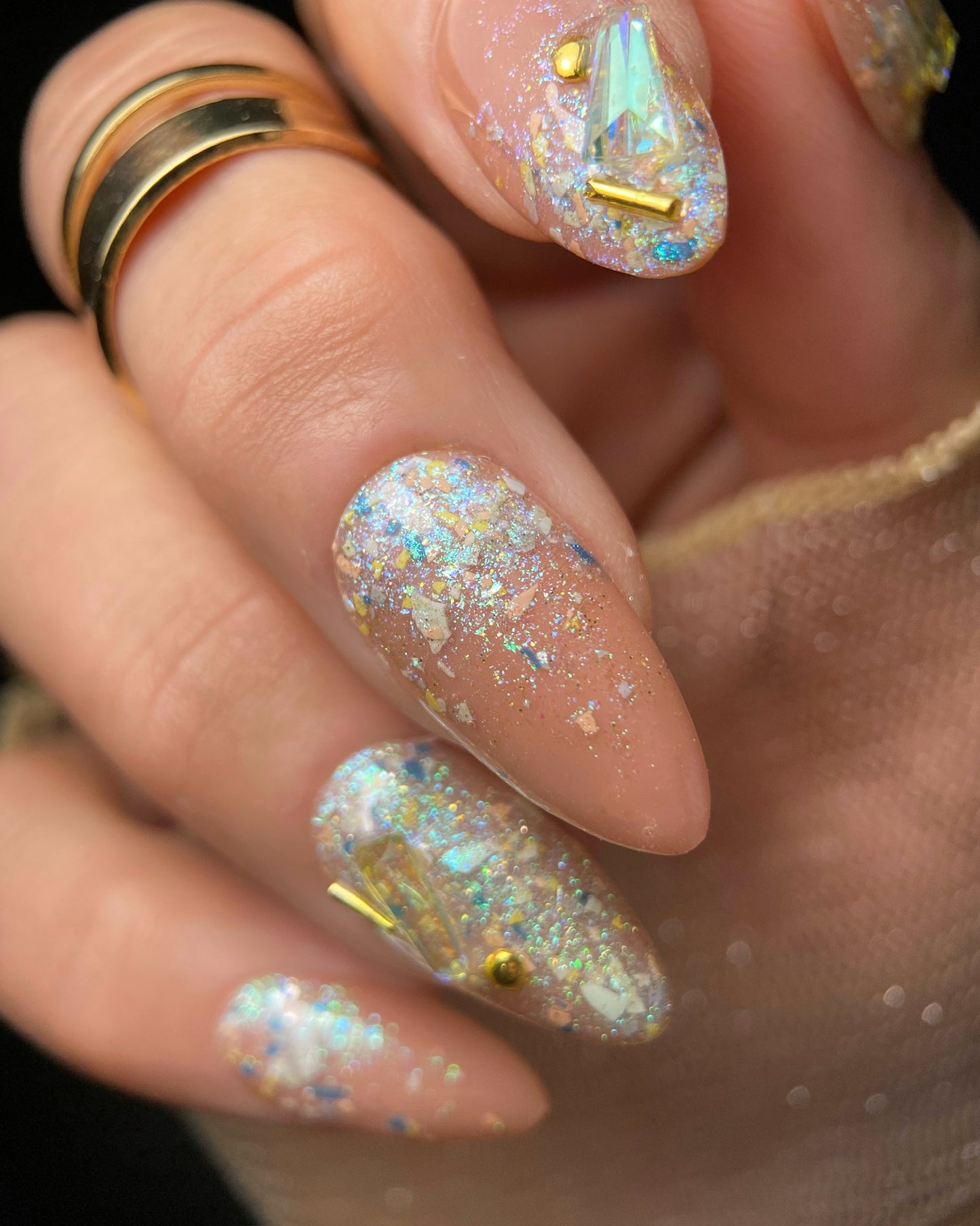 Close-up of a hand with glittery nail polish and gold rings.