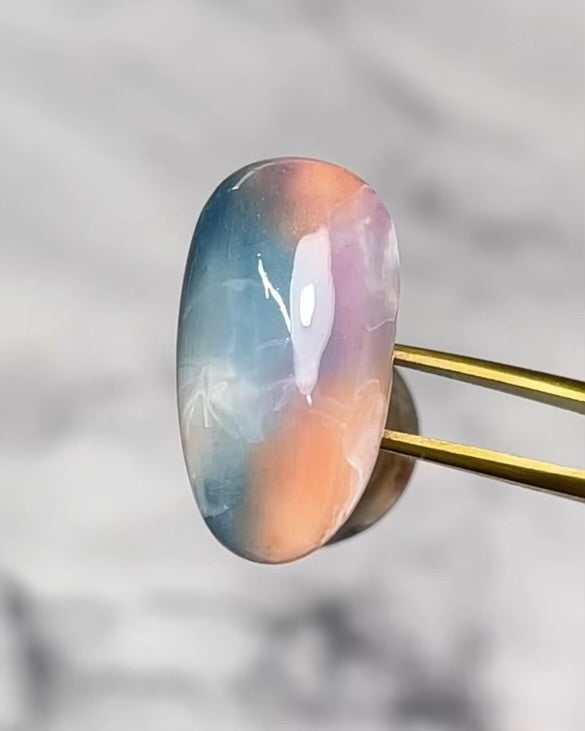 Tweezers holding decorated nail tip against blurred background