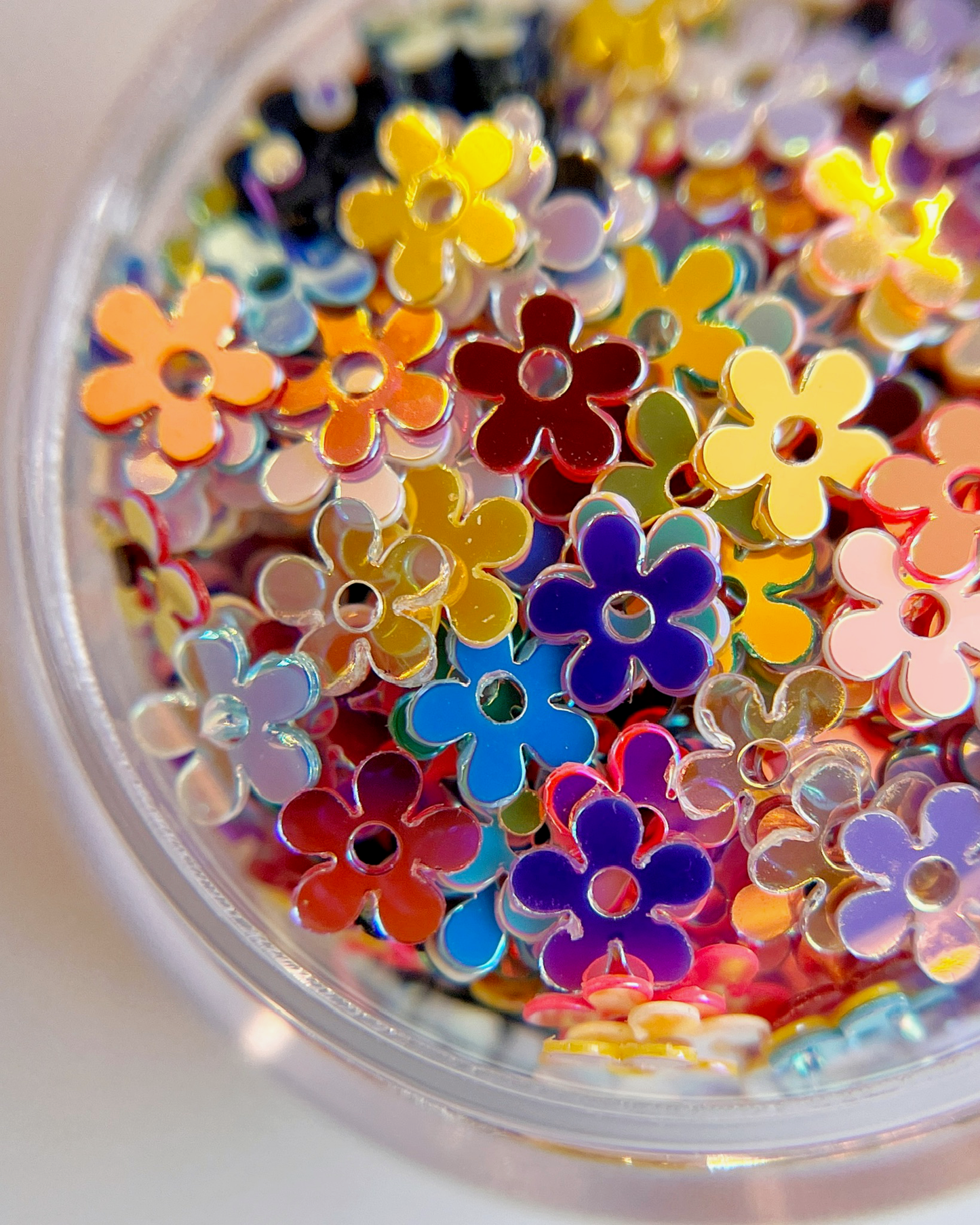 Detail view flower shaped nail glitter in clear jar on white background