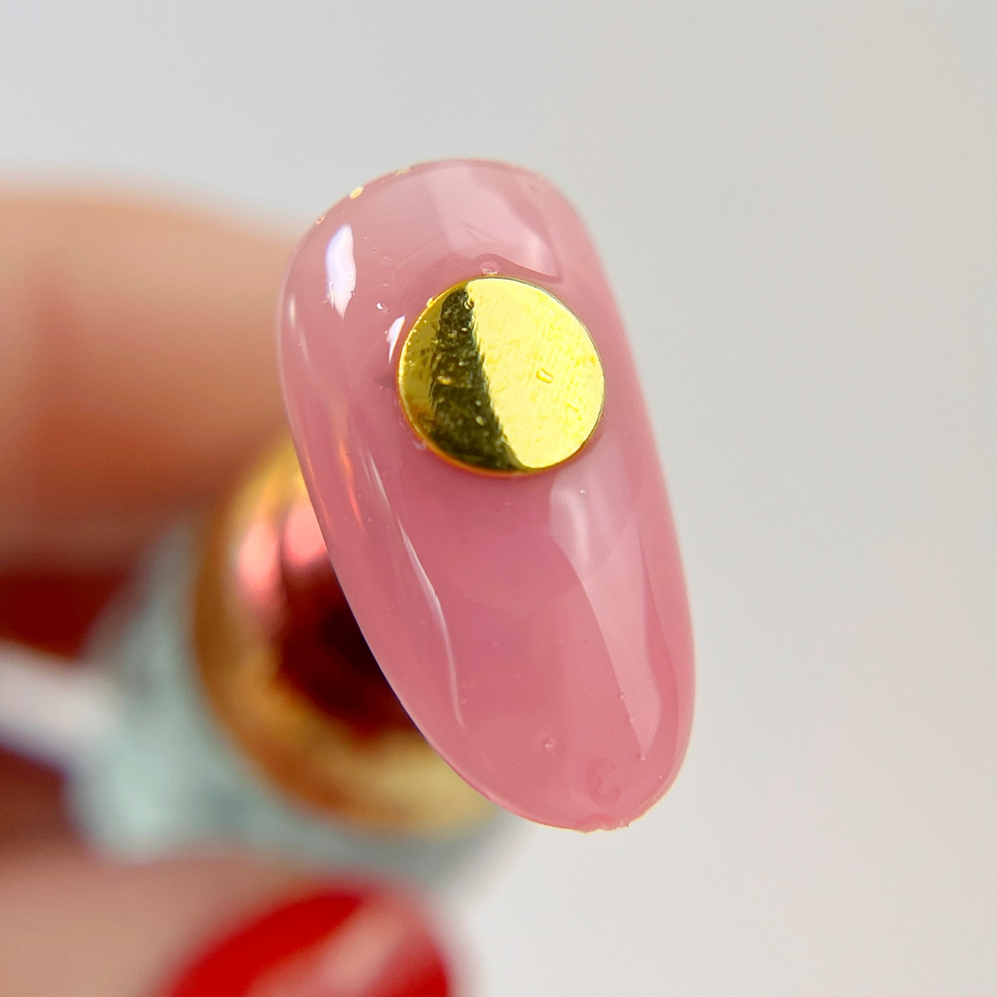 Hand hoding nail tip with round gold charm on white background.