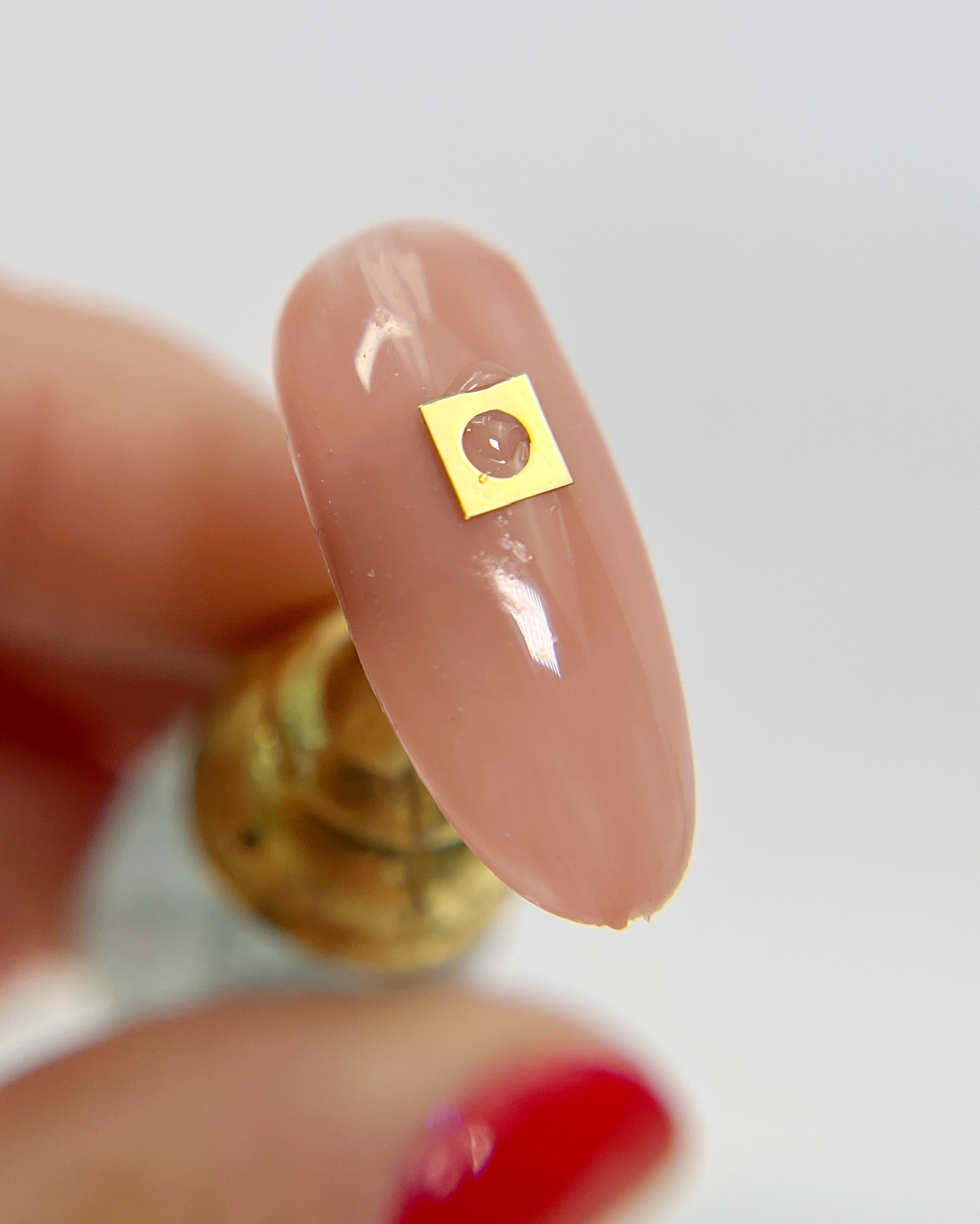 Hand holding decorated nail tip on white background.
