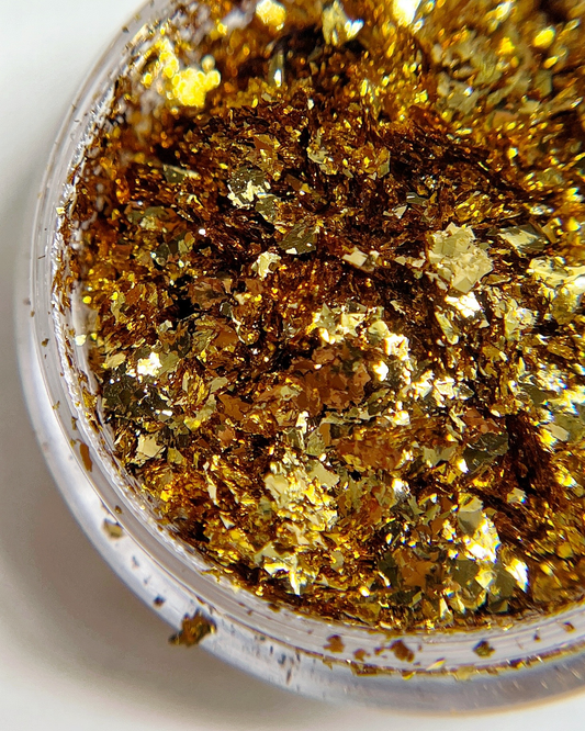 Thin gold foil flakes in clear jar on white background.