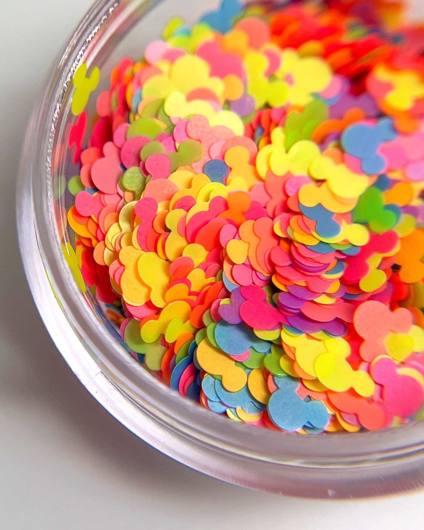 Detail view of multi color mouse shaped glitter in clear jar on white baclground.