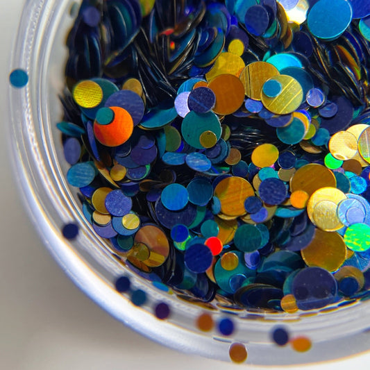 Multicolor round glitter in blue and gold colors in clear jar on white background.