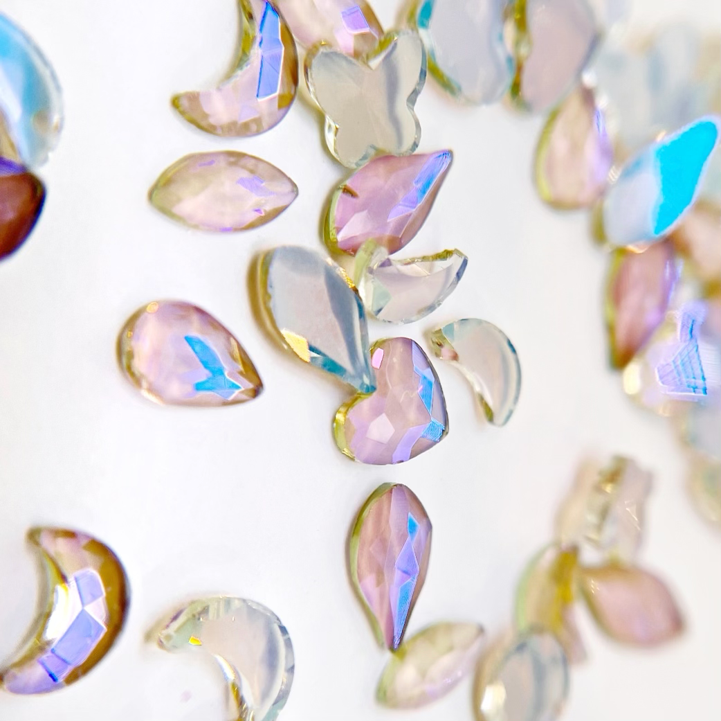 Multi shape iridescrnt rhinestones scattered on a white background.
