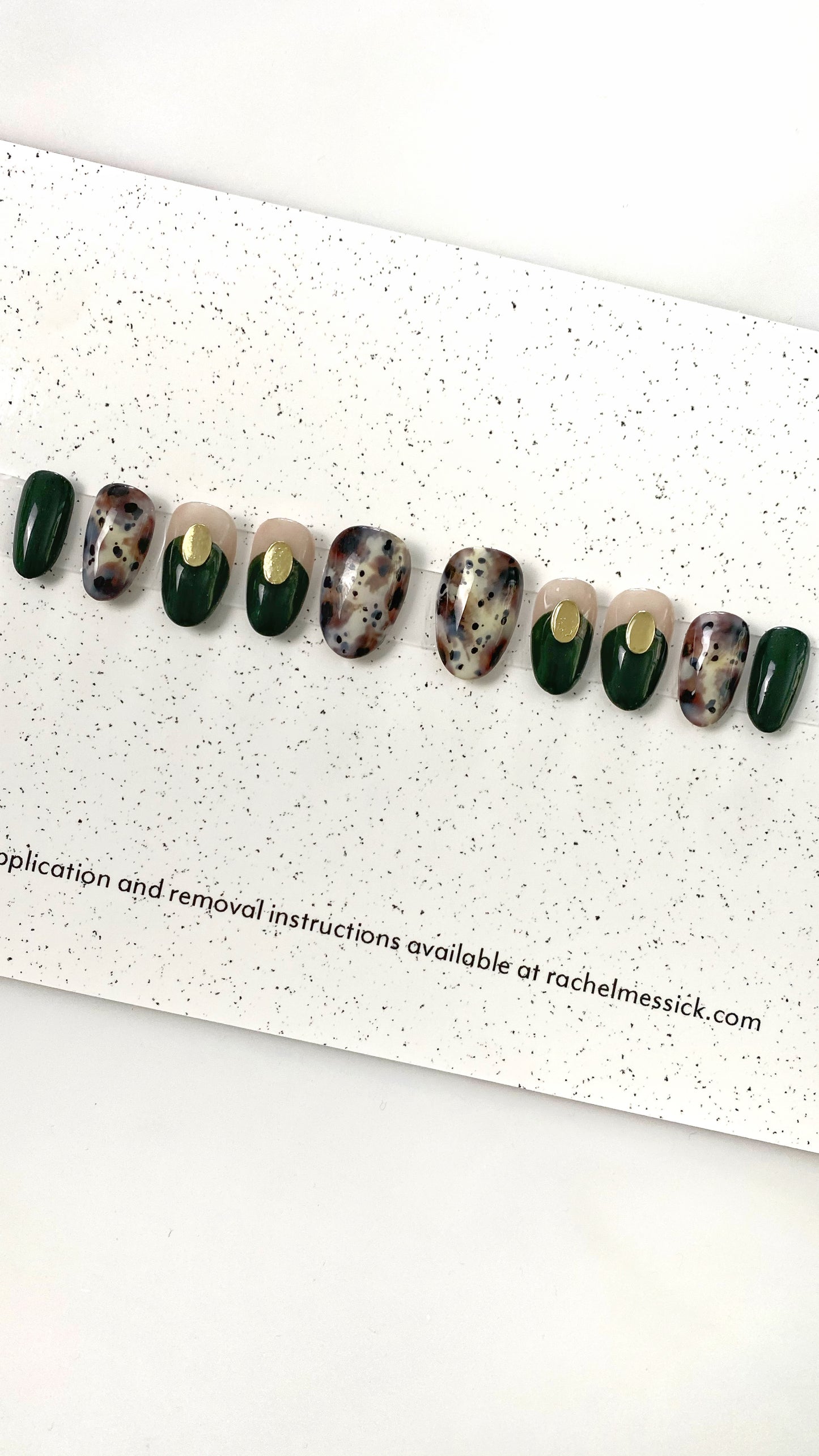 Multicolor nail tips with gold oval charms on speckled paper.