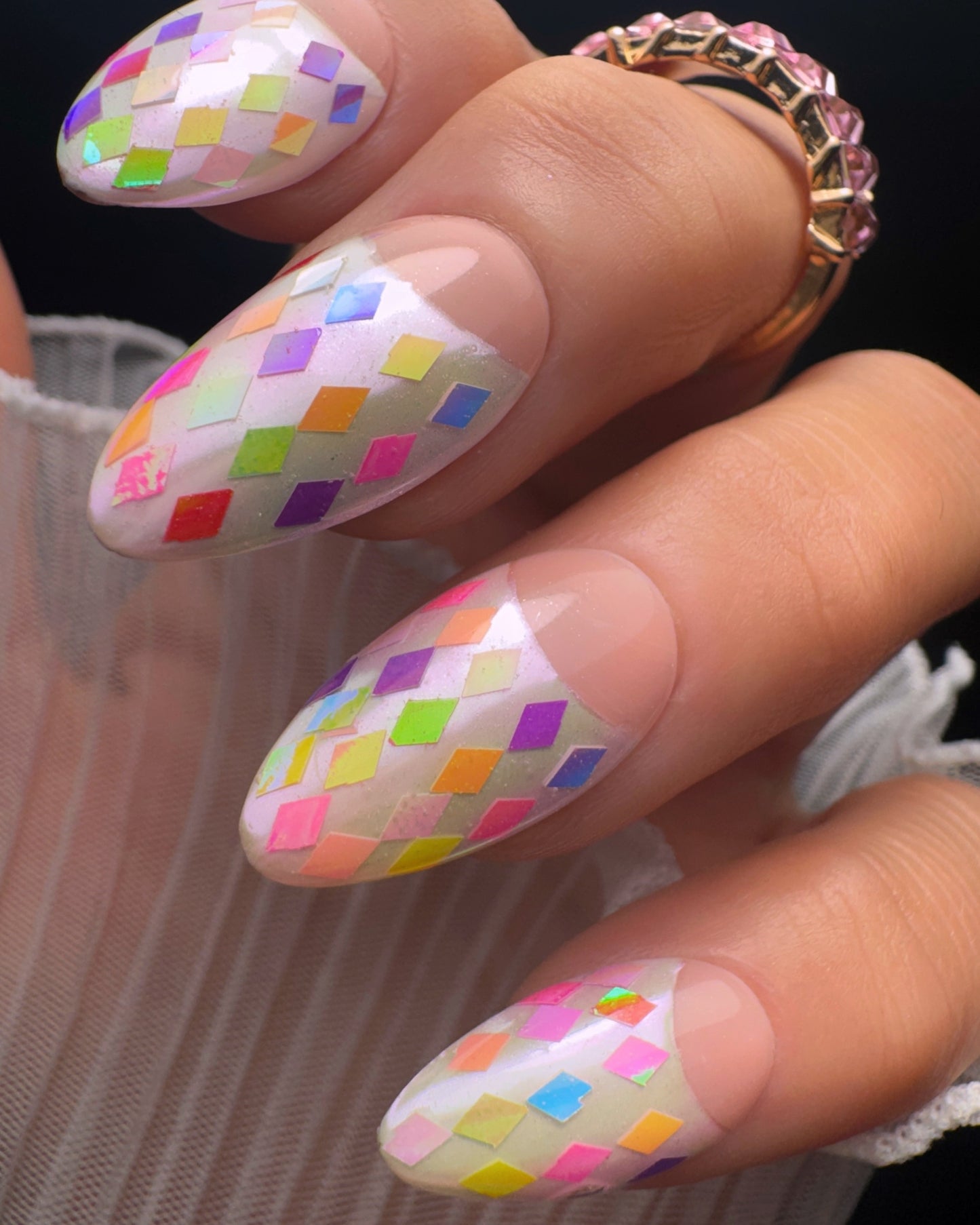 Nails with colorful diamond pattern on a hand wearing a ring.