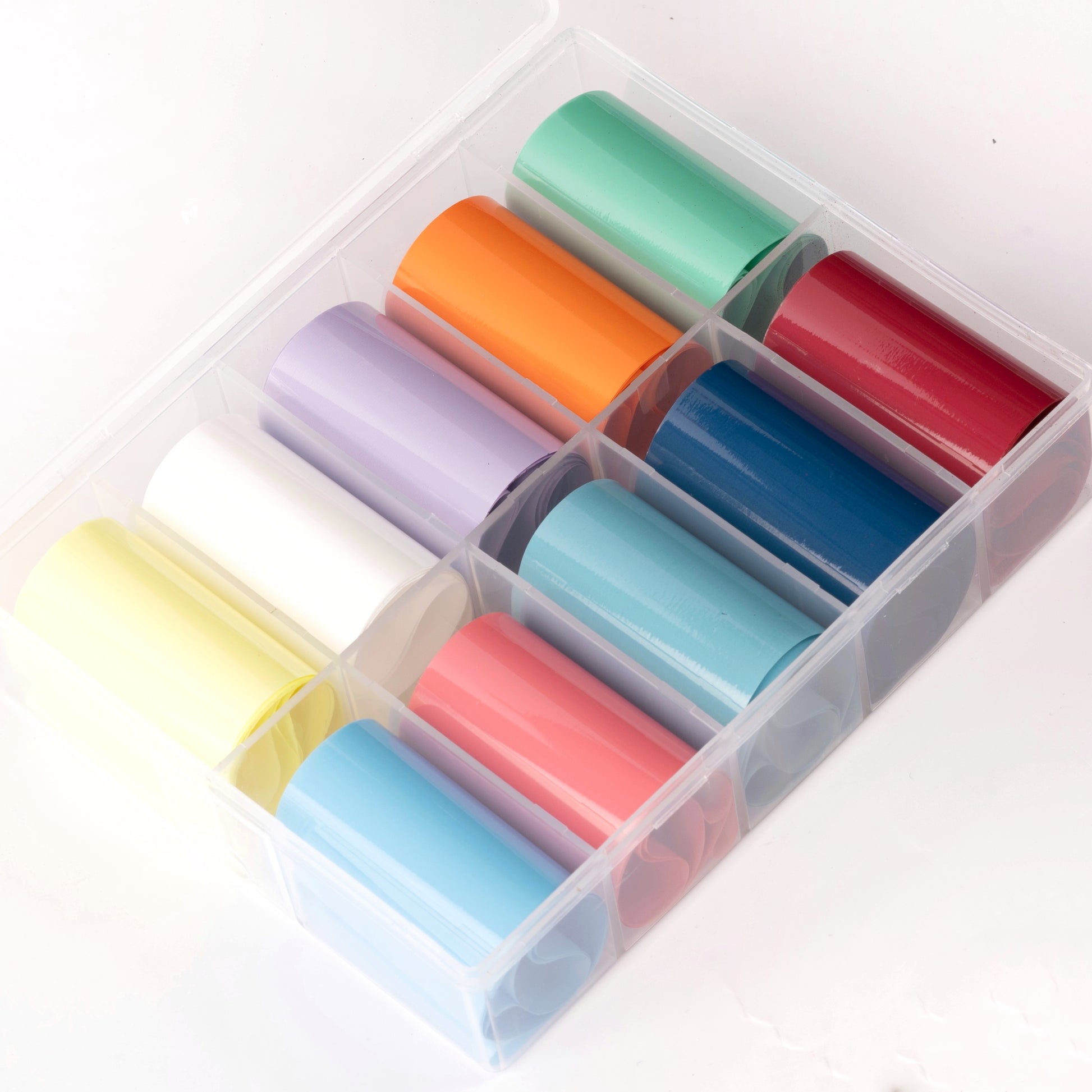 Multicolor rolls of transfer foil in clear case on white background.